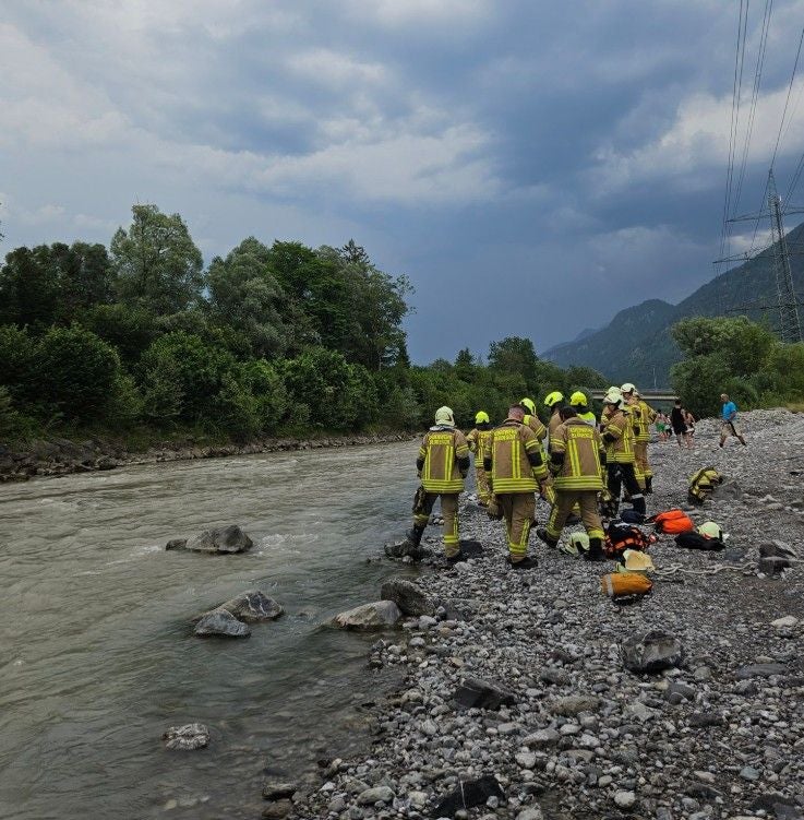 Feuerwehrleute stehen am Flussufer bei einem Einsatz nach einem Badeunfall.