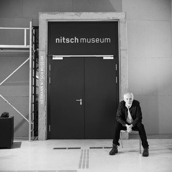 Ein älterer Mann sitzt vor dem Eingang des Nitsch Museums auf einem Stuhl.