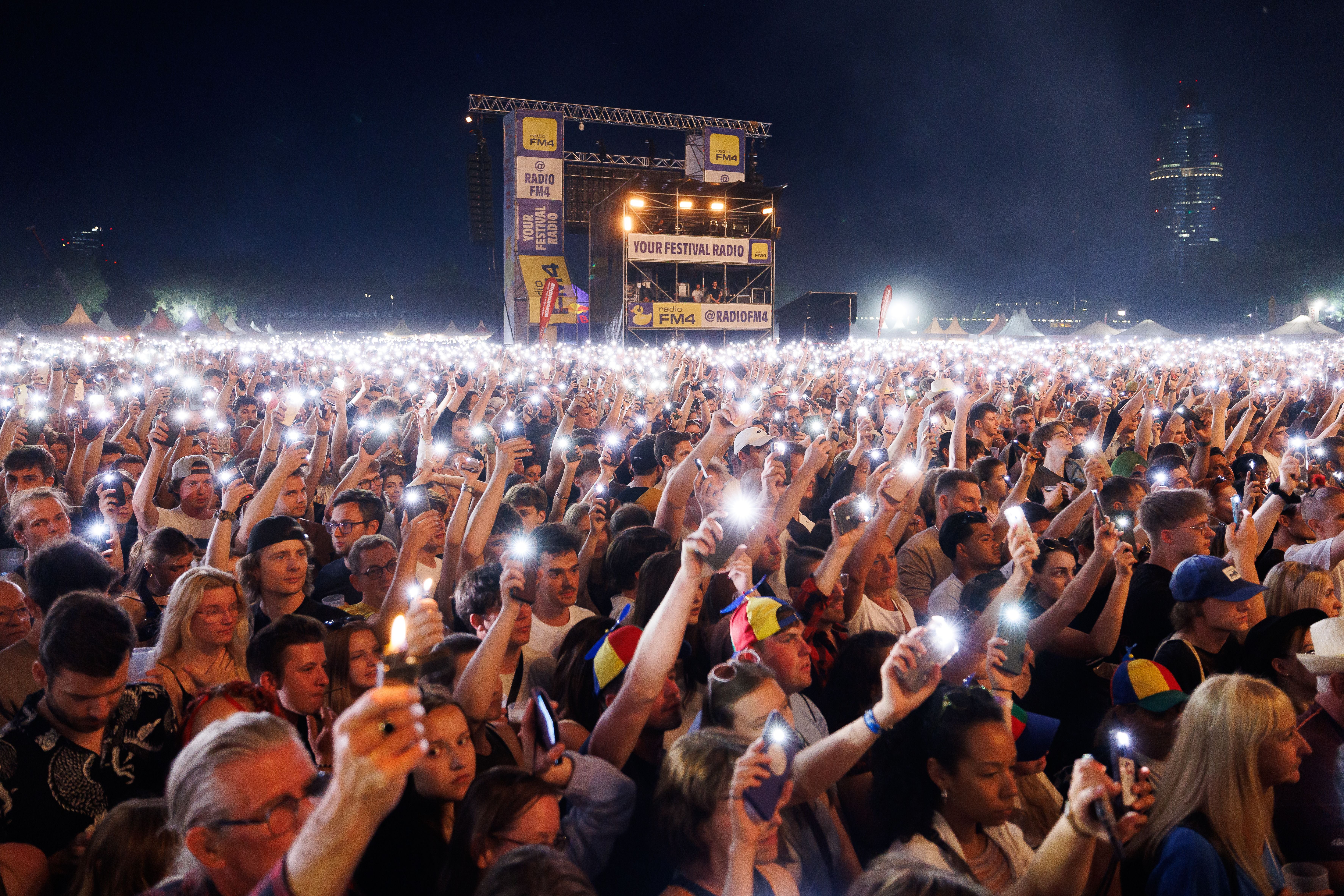 Menschenmenge hält leuchtende Handys in die Höhe bei einem Lichtermeer auf dem Donauinselfest in Wien.