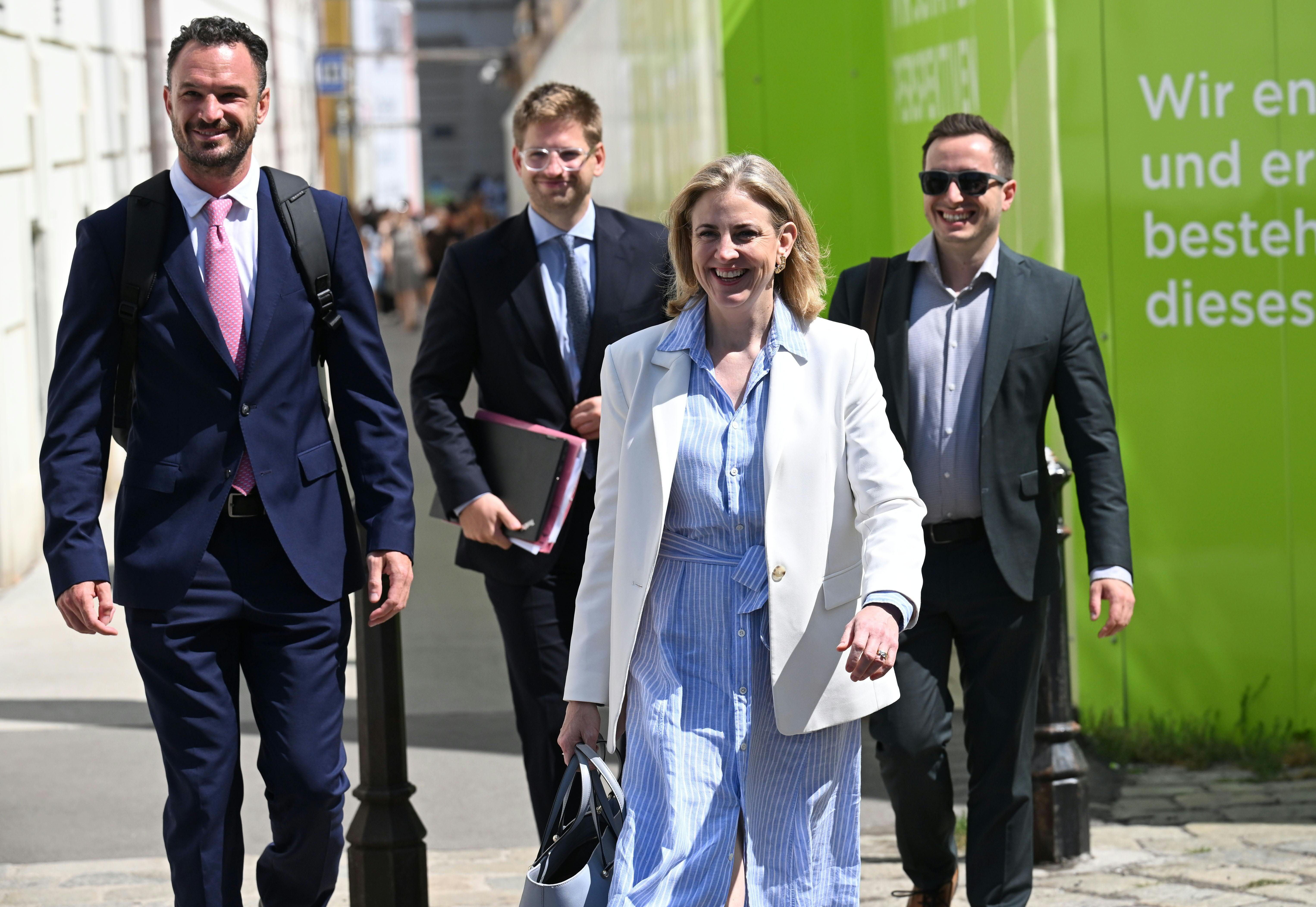 Vier Personen in Businesskleidung gehen lächelnd draußen in der Sonne in Wien.