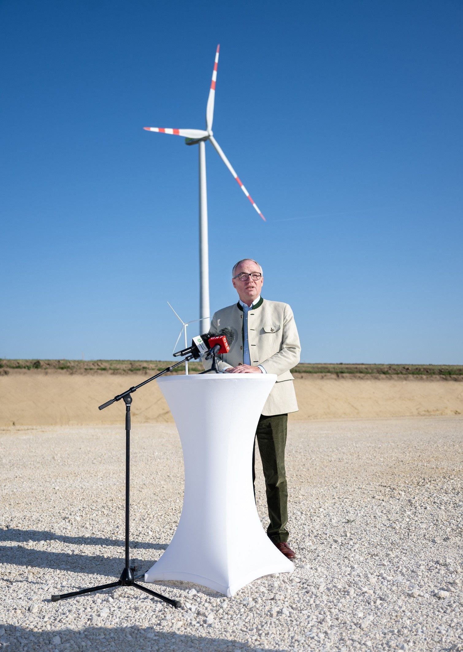 Ein Mann hält eine Rede vor einem Windrad im Freien bei sonnigem Wetter.