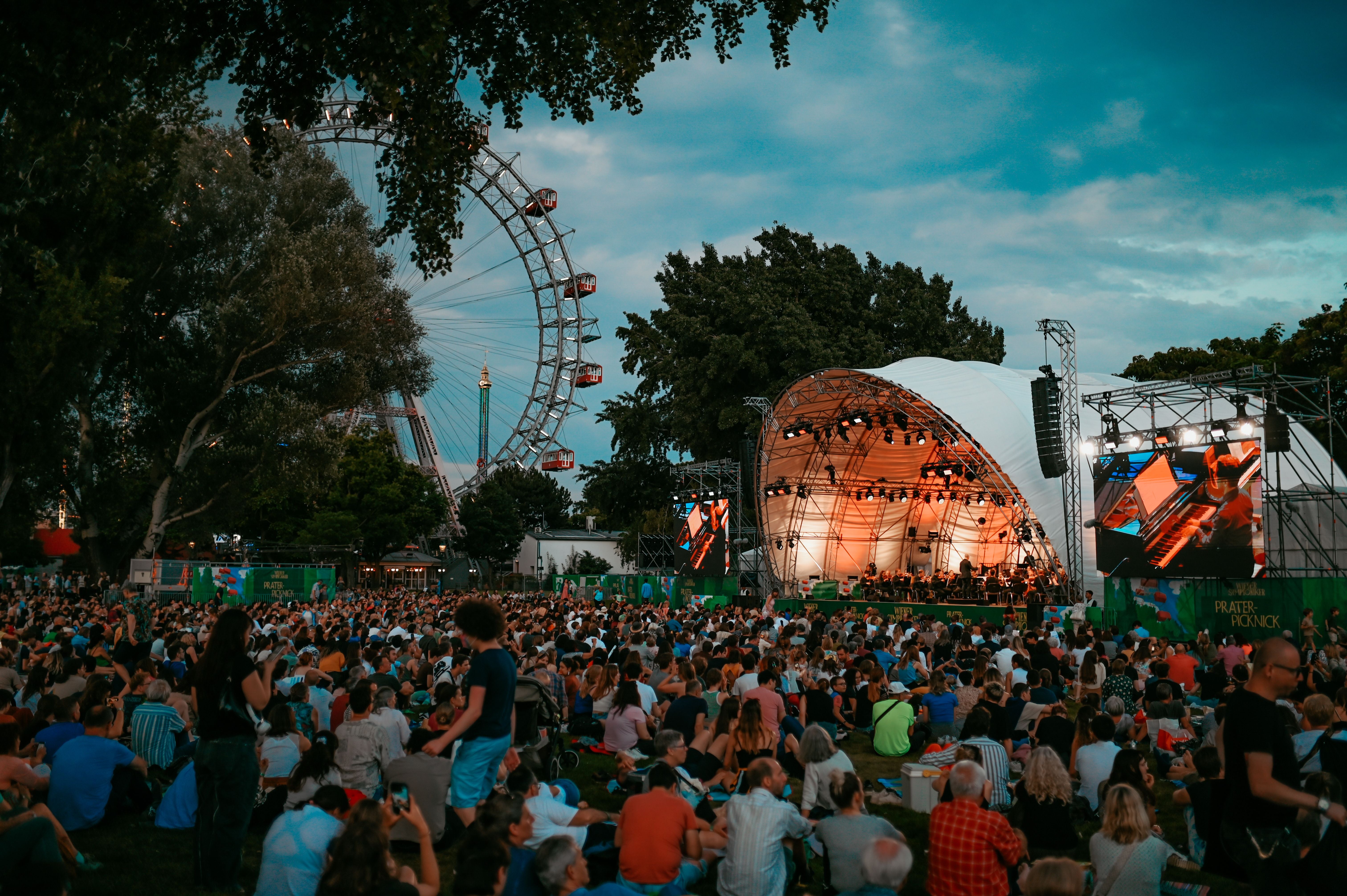 Viele Menschen sitzen auf einer Wiese vor einer Open-Air-Bühne im Wiener Prater.