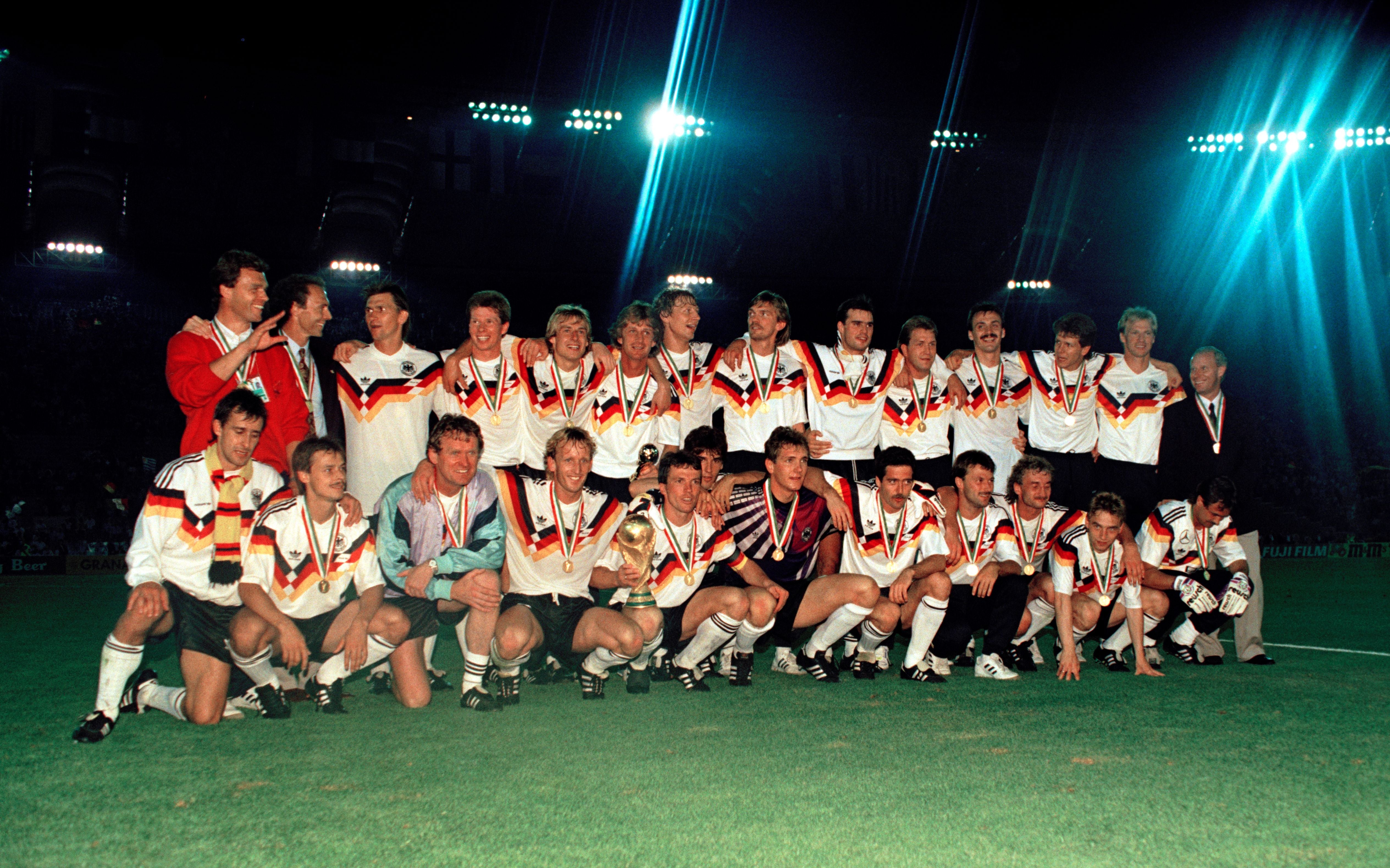 ROME, ITALY - JULY 8: West Germany line up for a group photo as they celebrate with the trophy after the FIFA World Cup final between West Germany and Argentina at the Stadio Olimpico on July 8, 1990 in Rome, Italy. West Germany won 1-0. Back row (left-right): Holger Osieck (assistant coach), Franz Beckenbauer (manager), Klaus Augenthaler, Stefan Reuter, Jurgen Klinsmann, Frank Mill, Guido Buchwald, Paul Steiner, Thomas Berthold, Andreas Kopke, Jurgen Kohler, Andreas Moller, Hans Pflugler and Berti Vogts (assistant manager). Front row: Pierre Littbarski, Olaf Thon, Sepp Maier (goalkeeping coach), Andreas Brehme, Lothar Matthaus, Karl-Heinz Riedle, Bodo Illgner, Uwe Bein, Gunter Hermann, Rudi Voller, Thomas Haessler and Raimond Aumann. (Photo by Paul Popper/Popperfoto via Getty Images)