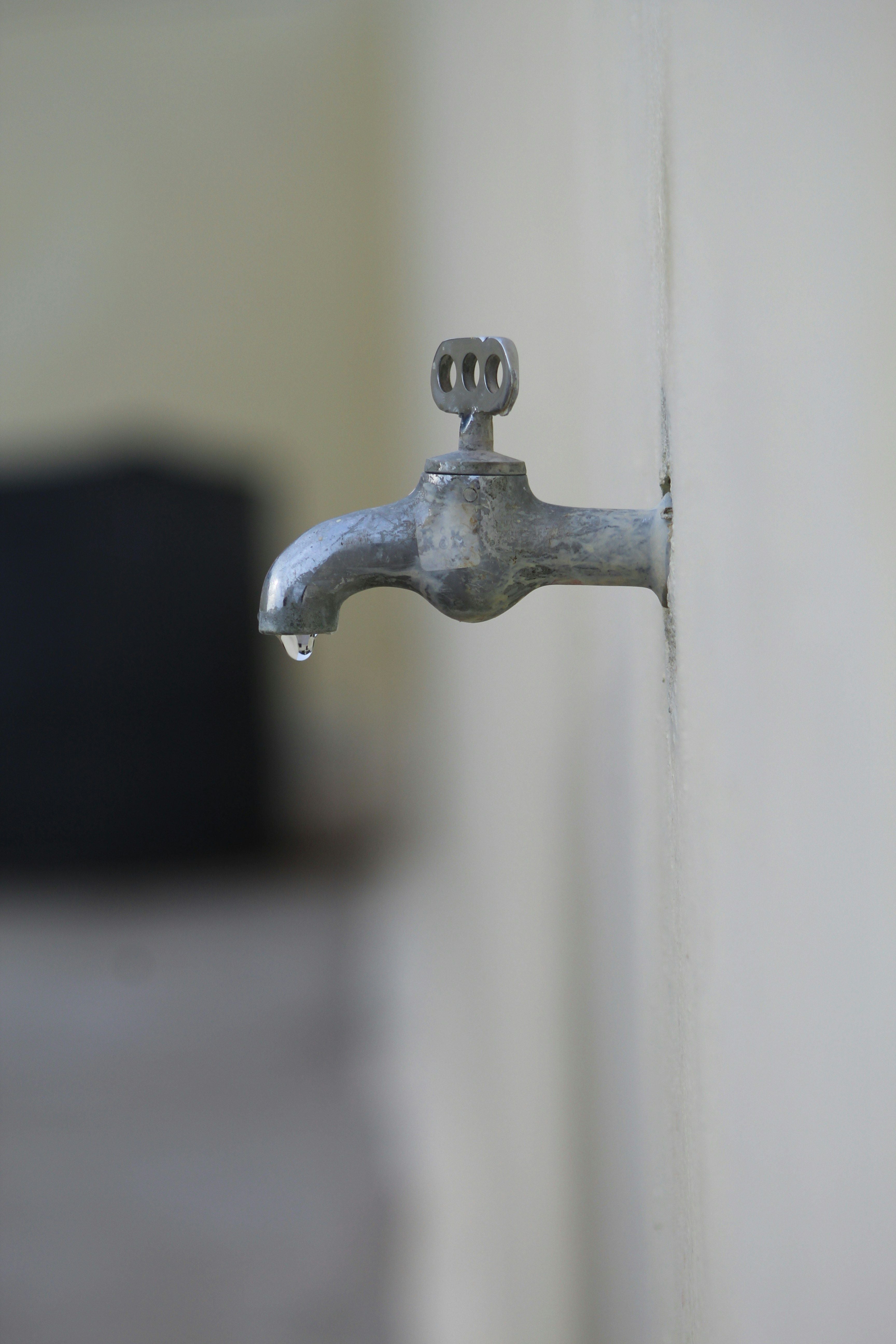 Metallwasserhahn an einer Wand mit einem herabfallenden Wassertropfen.