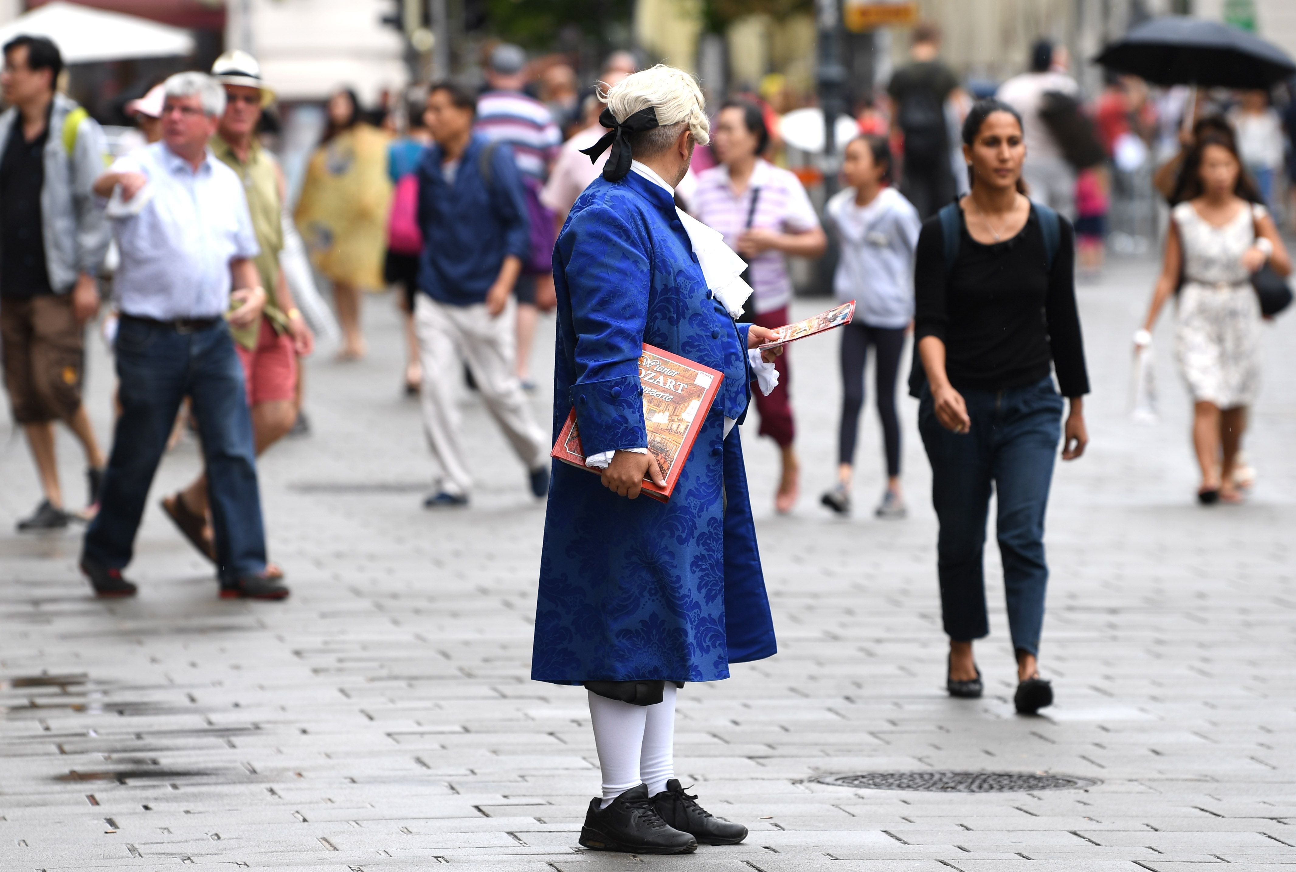 Ein Ticketverkäufer im blauen Mozartkostüm steht vor der Wiener Staatsoper in einer Menschenmenge.