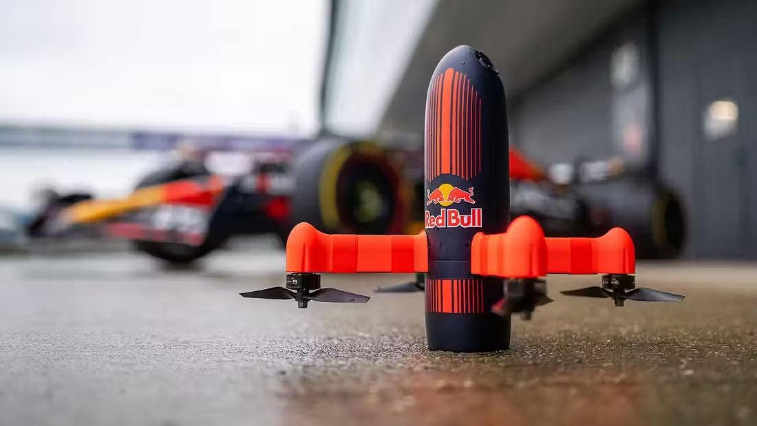 Eine Red Bull Drohne steht am Boden vor einem Formel-1-Rennwagen.