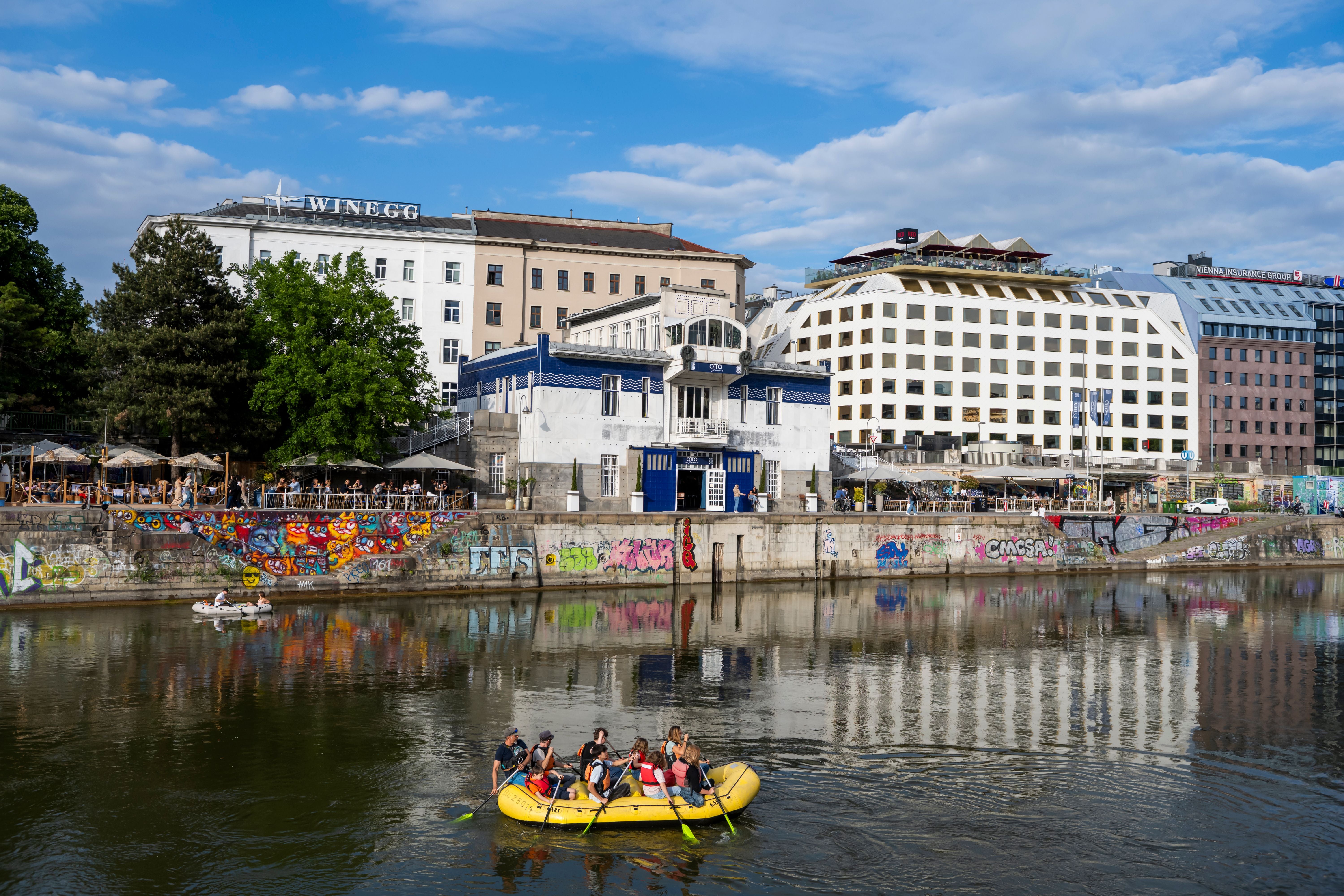 Eine Gruppe von Menschen fährt in einem gelben Schlauchboot auf dem Donaukanal in Wien.