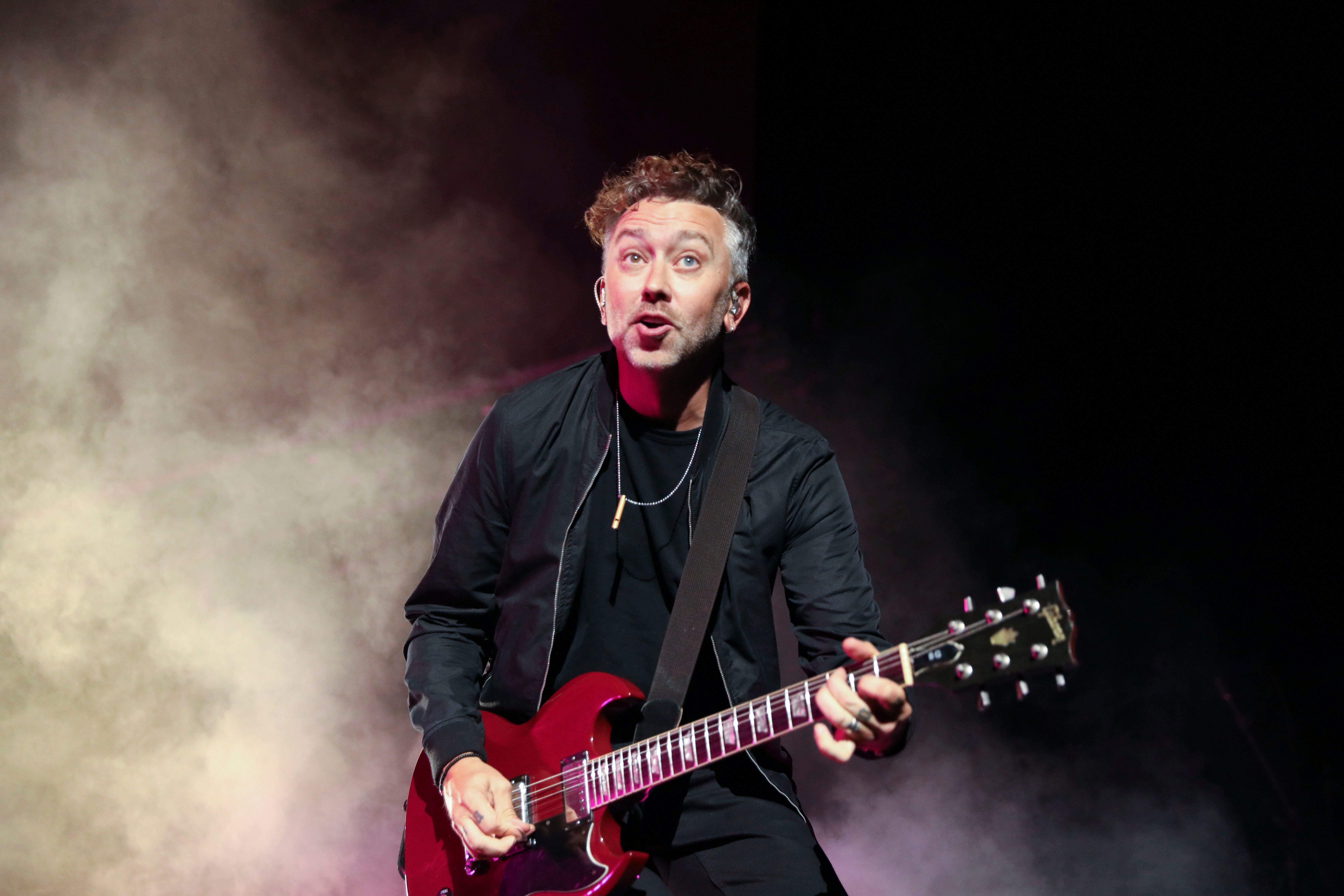 Ein Musiker spielt E-Gitarre auf einer Bühne im Scheinwerferlicht mit Nebel im Hintergrund.
