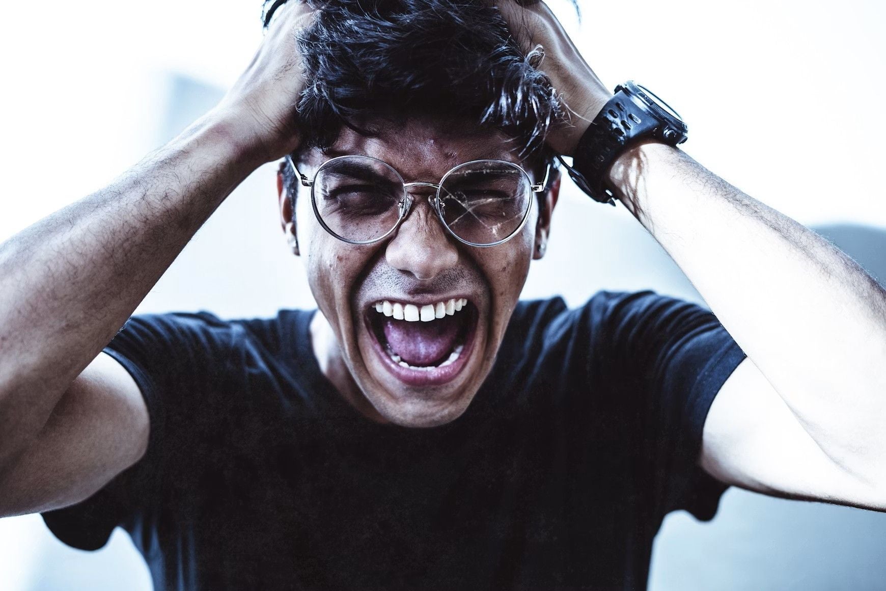 Mann mit Brille schreit und greift sich frustriert an die Haare.