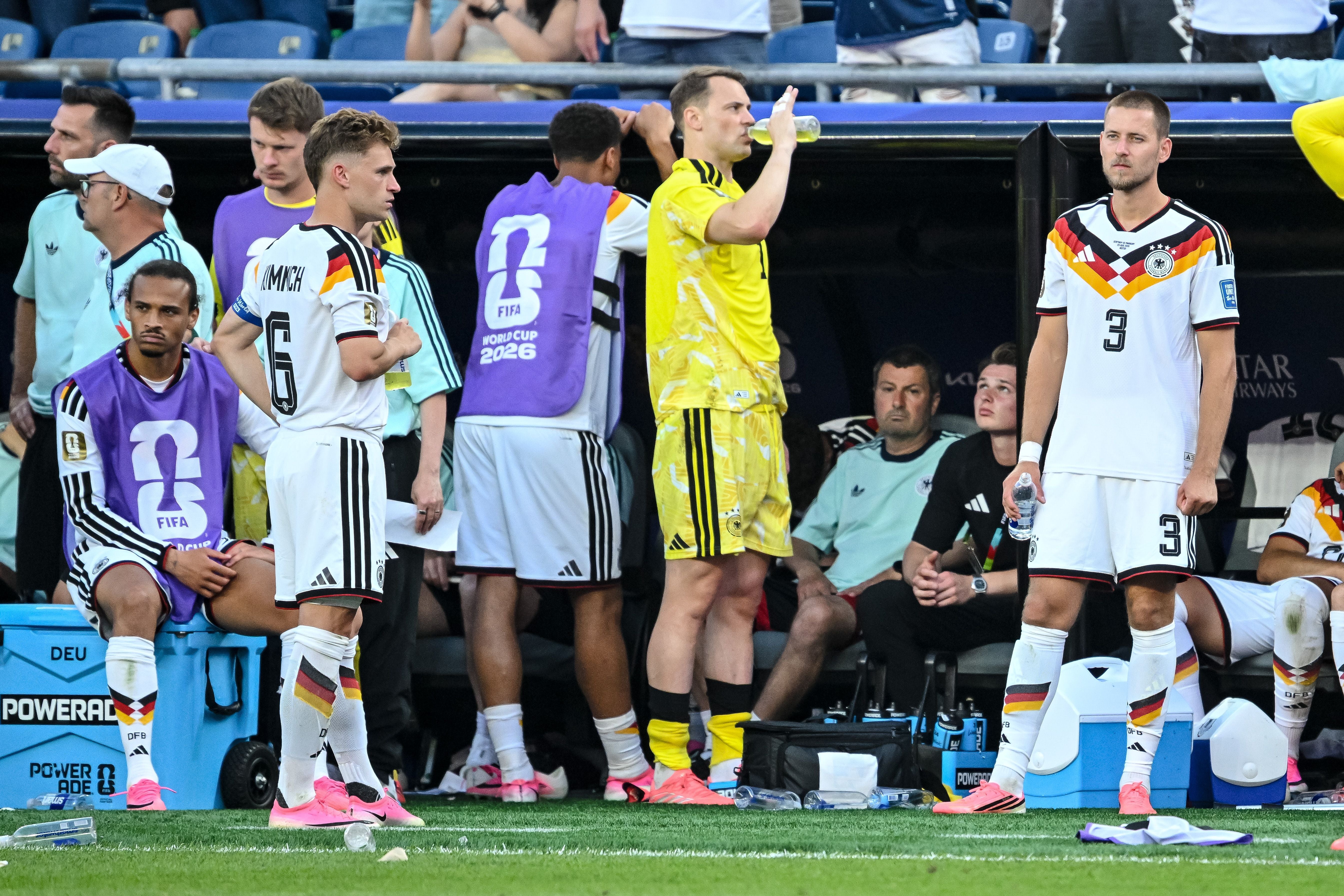 Deutsche Fußballspieler sitzen und stehen enttäuscht an der Ersatzbank während eines Spiels.