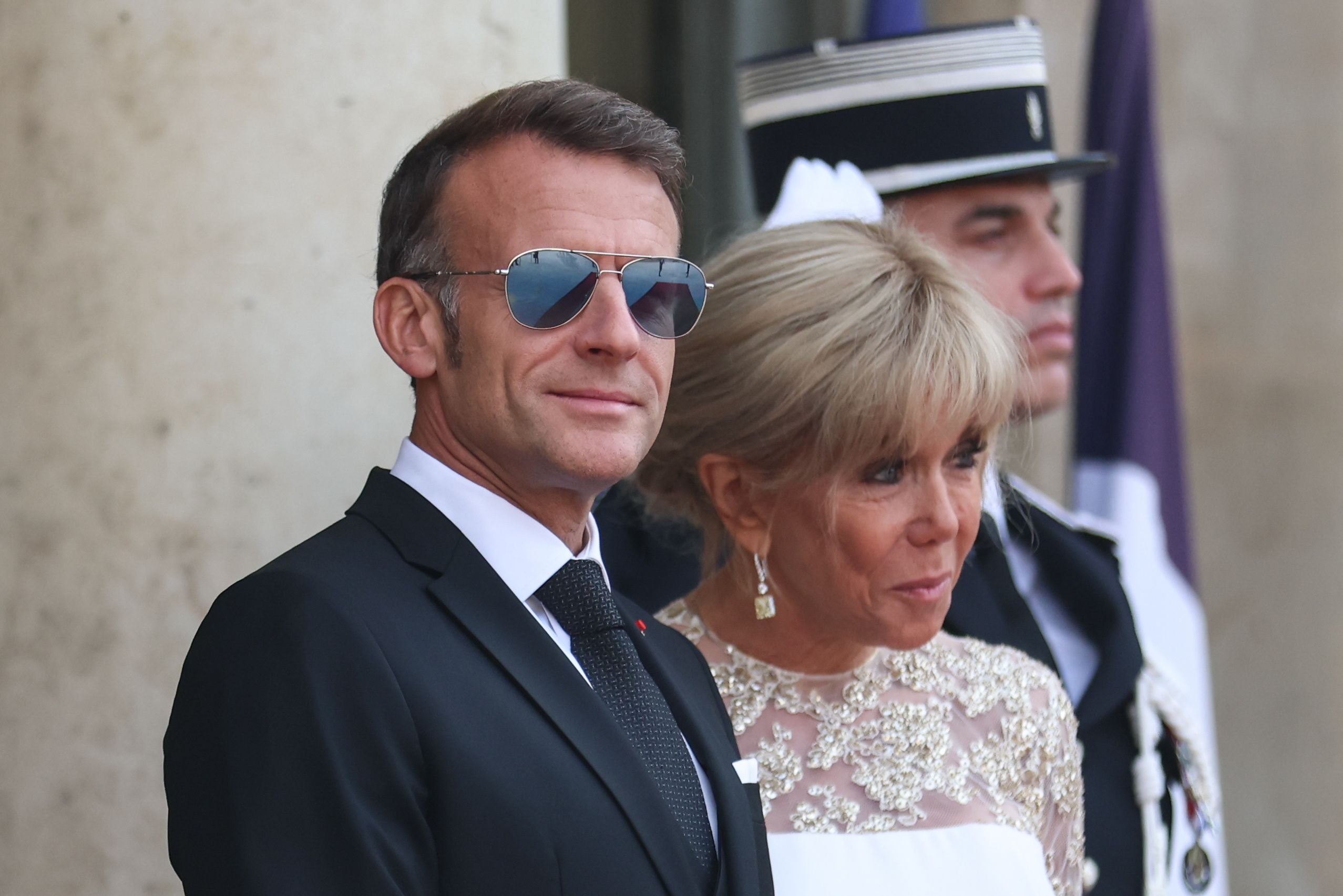 Ein Mann im Anzug mit Sonnenbrille steht neben einer Frau im festlichen Kleid.
