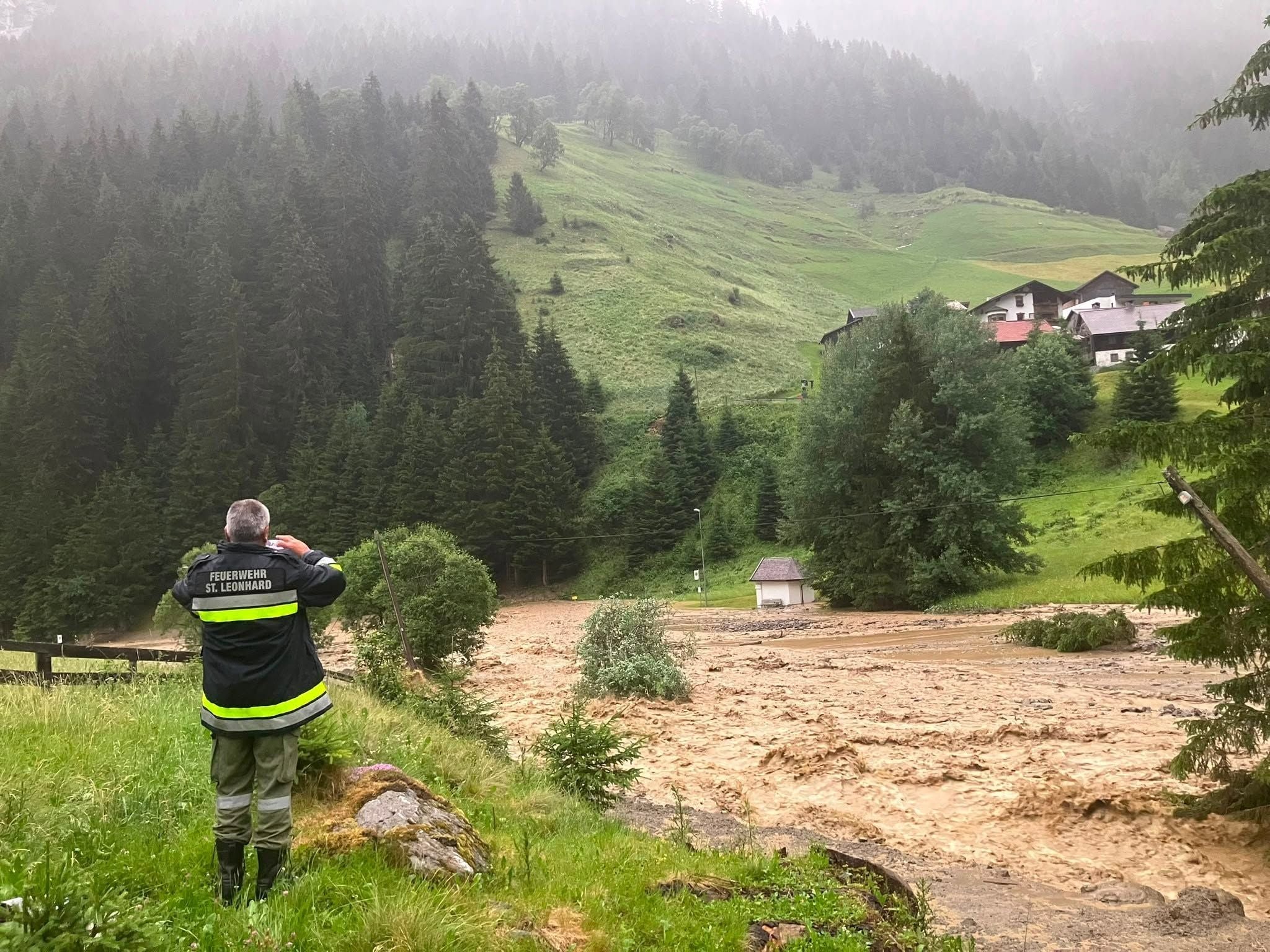 Ein Feuerwehrmann beobachtet ein überschwemmtes Flussbett in einer bergigen, ländlichen Gegend.