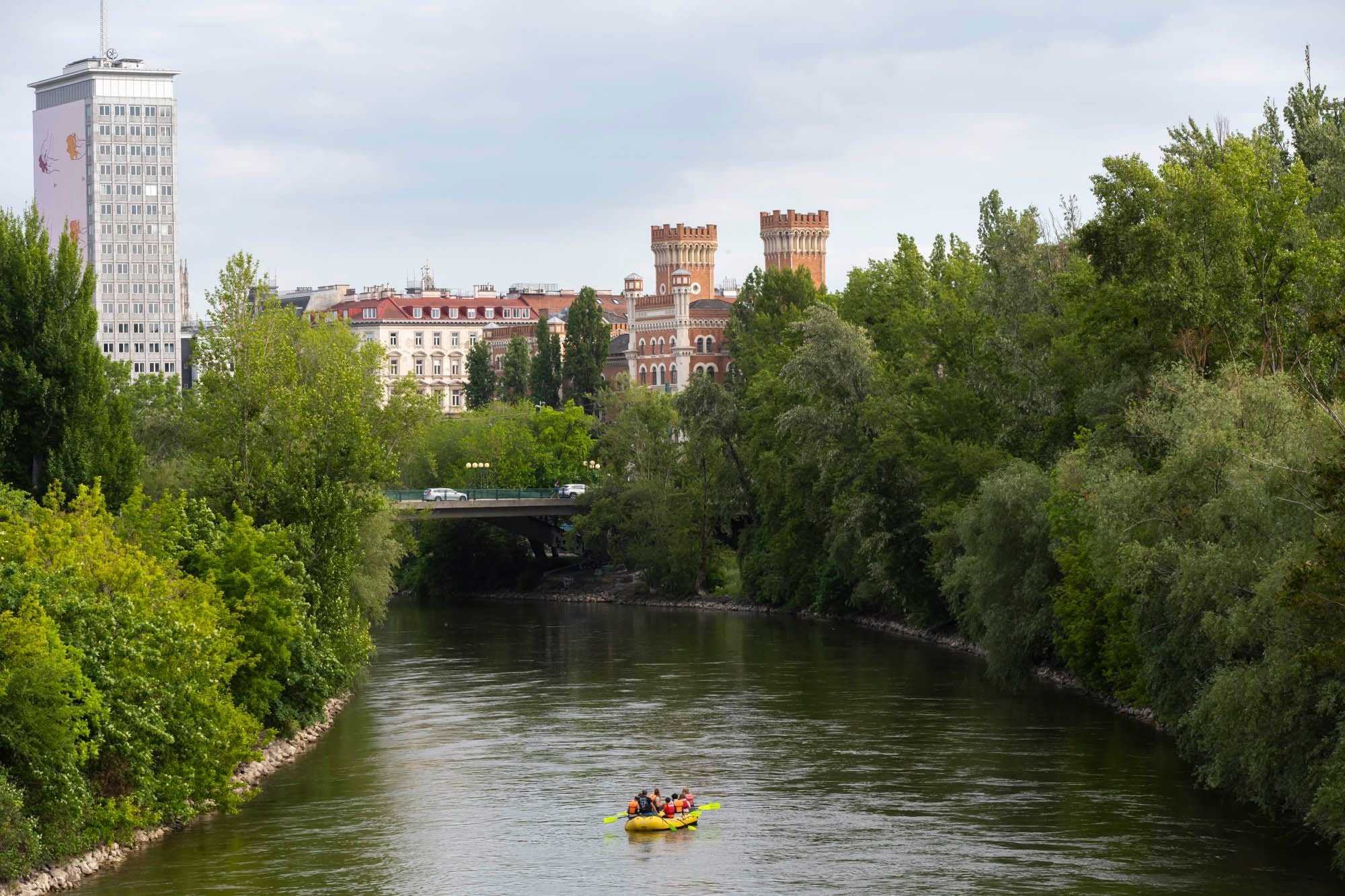 Mehrere Personen fahren in einem gelben Schlauchboot auf dem Donaukanal, umgeben von viel Grün.