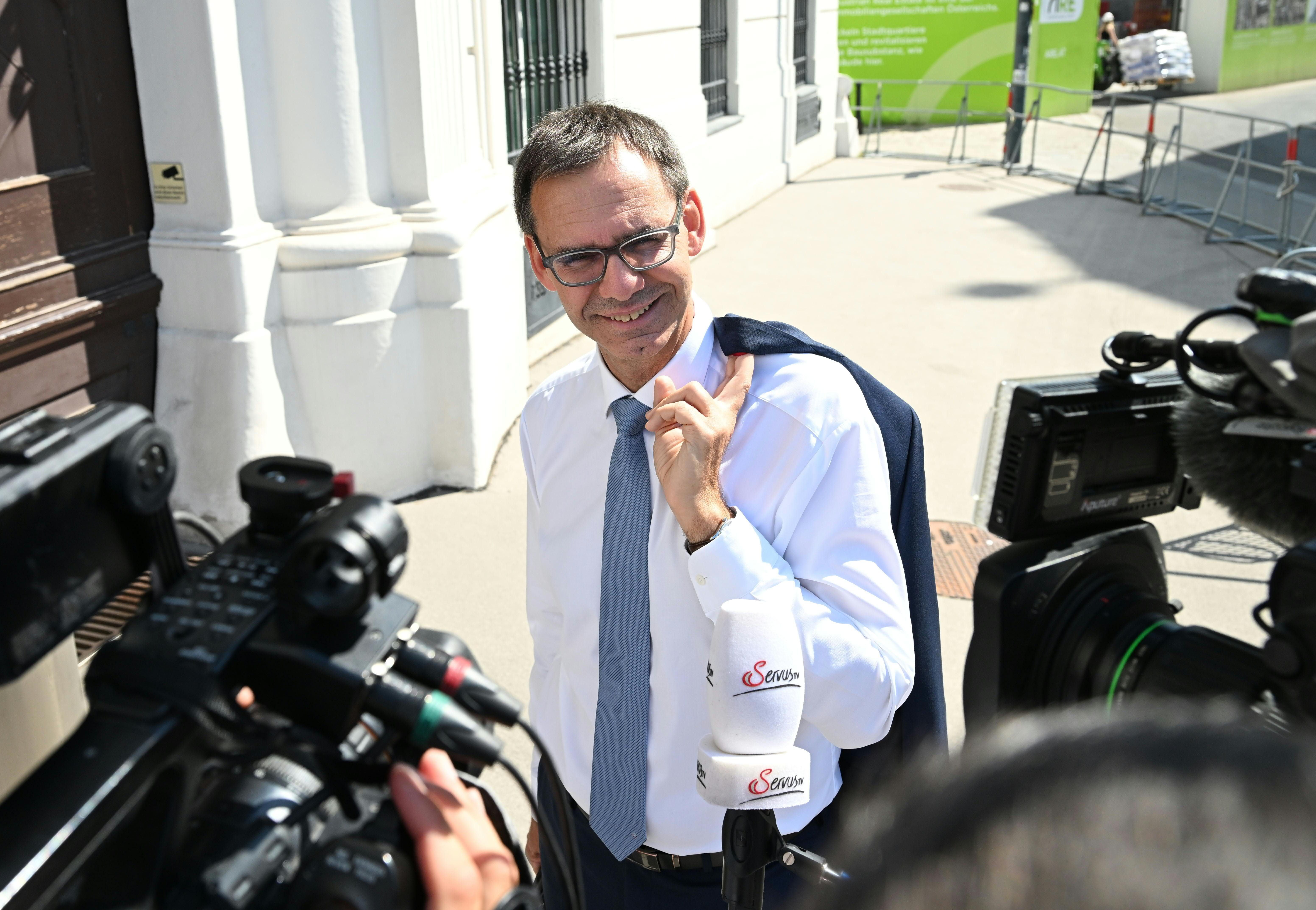 Ein Mann im Anzug gibt draußen vor Kameras und Mikrofonen ein Interview und lächelt.
