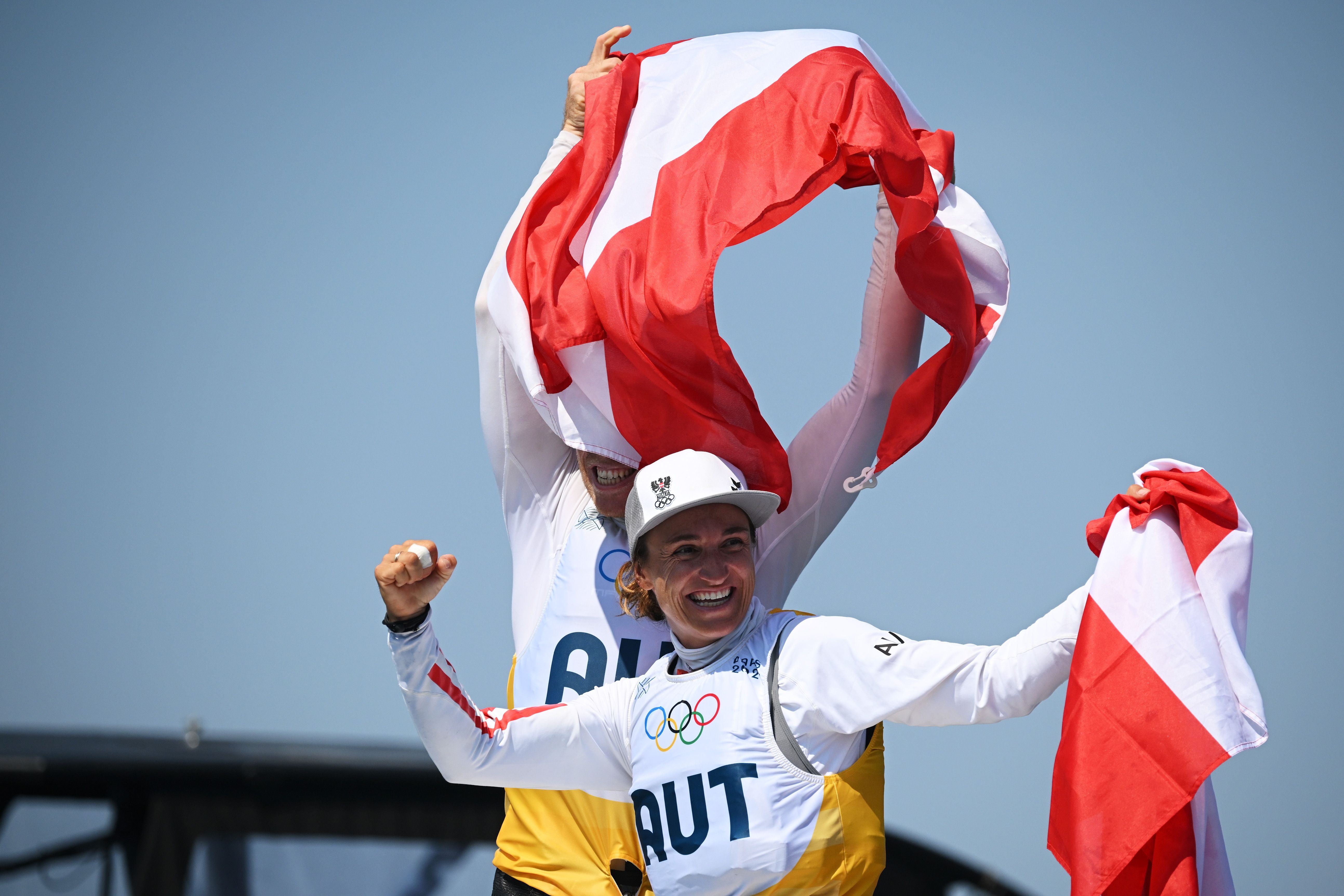 Zwei österreichische Segler jubeln mit rot-weißen Flaggen bei den Olympischen Spielen.