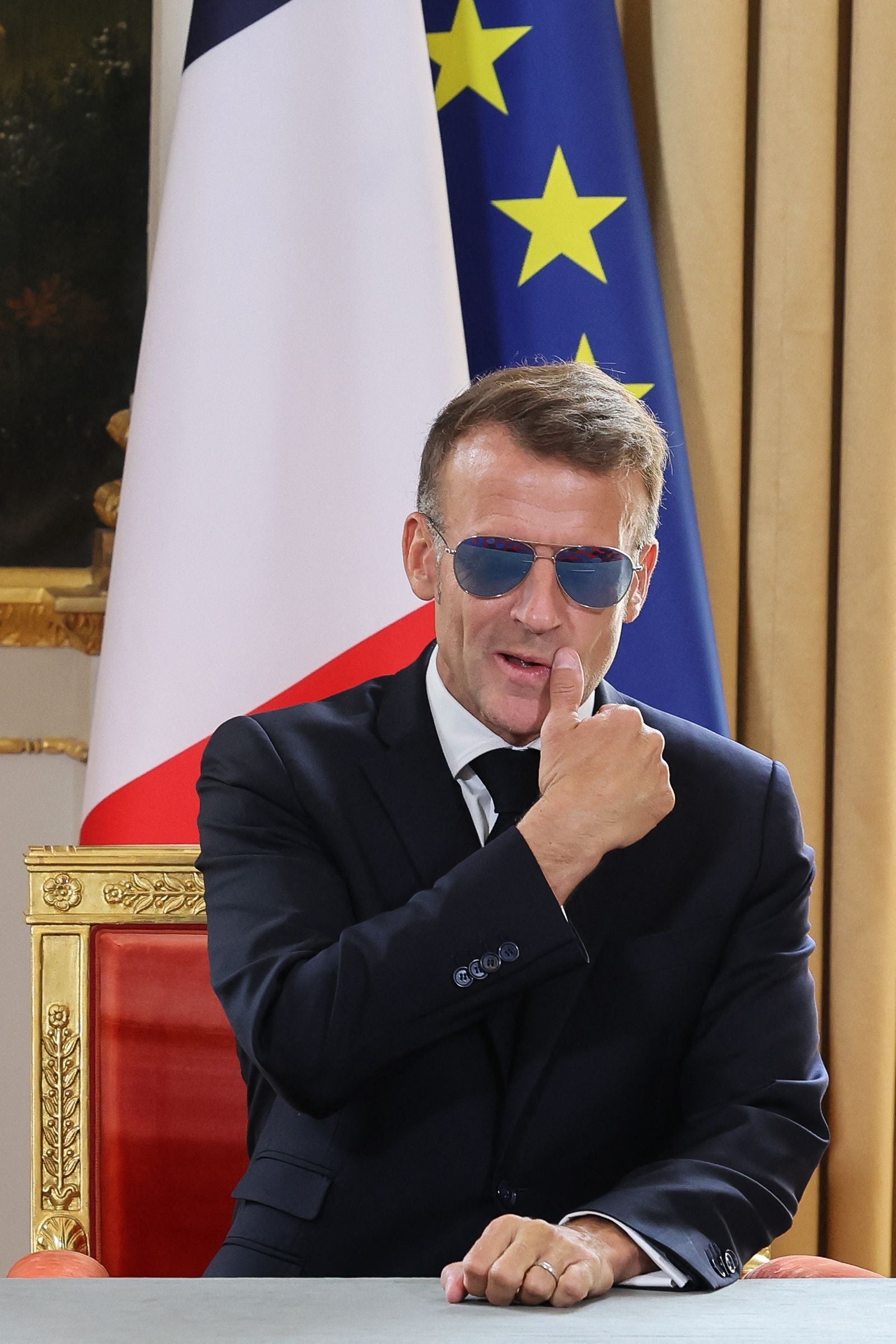 Ein Mann im Anzug mit Sonnenbrille zeigt Daumen hoch vor EU- und Frankreich-Flagge.