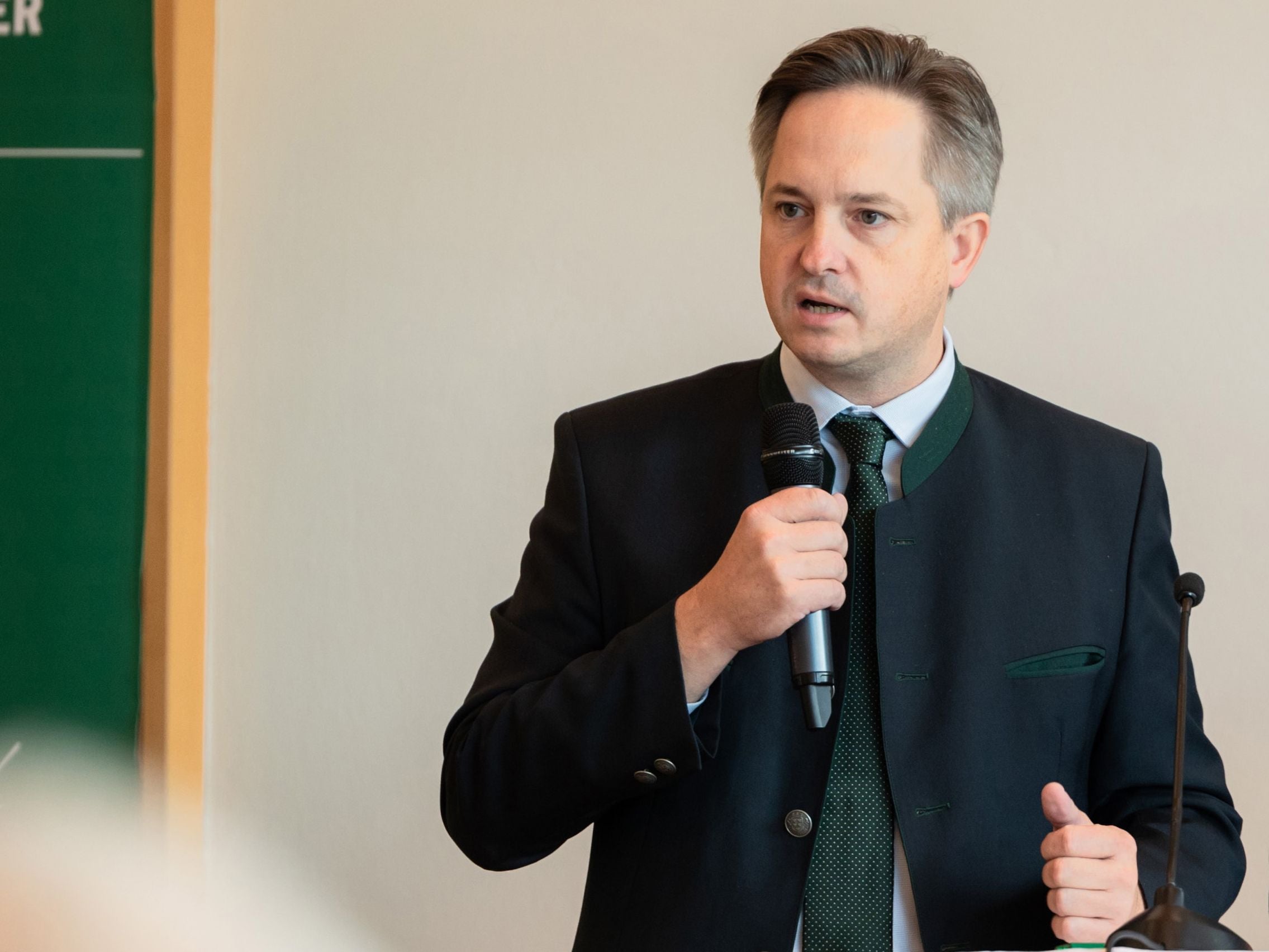 Ein Mann im Anzug spricht mit einem Mikrofon bei einer Veranstaltung.