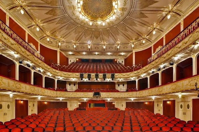 Blick auf den prunkvollen Innenraum des Stadttheaters Baden mit roten Sitzreihen und Balkonen.