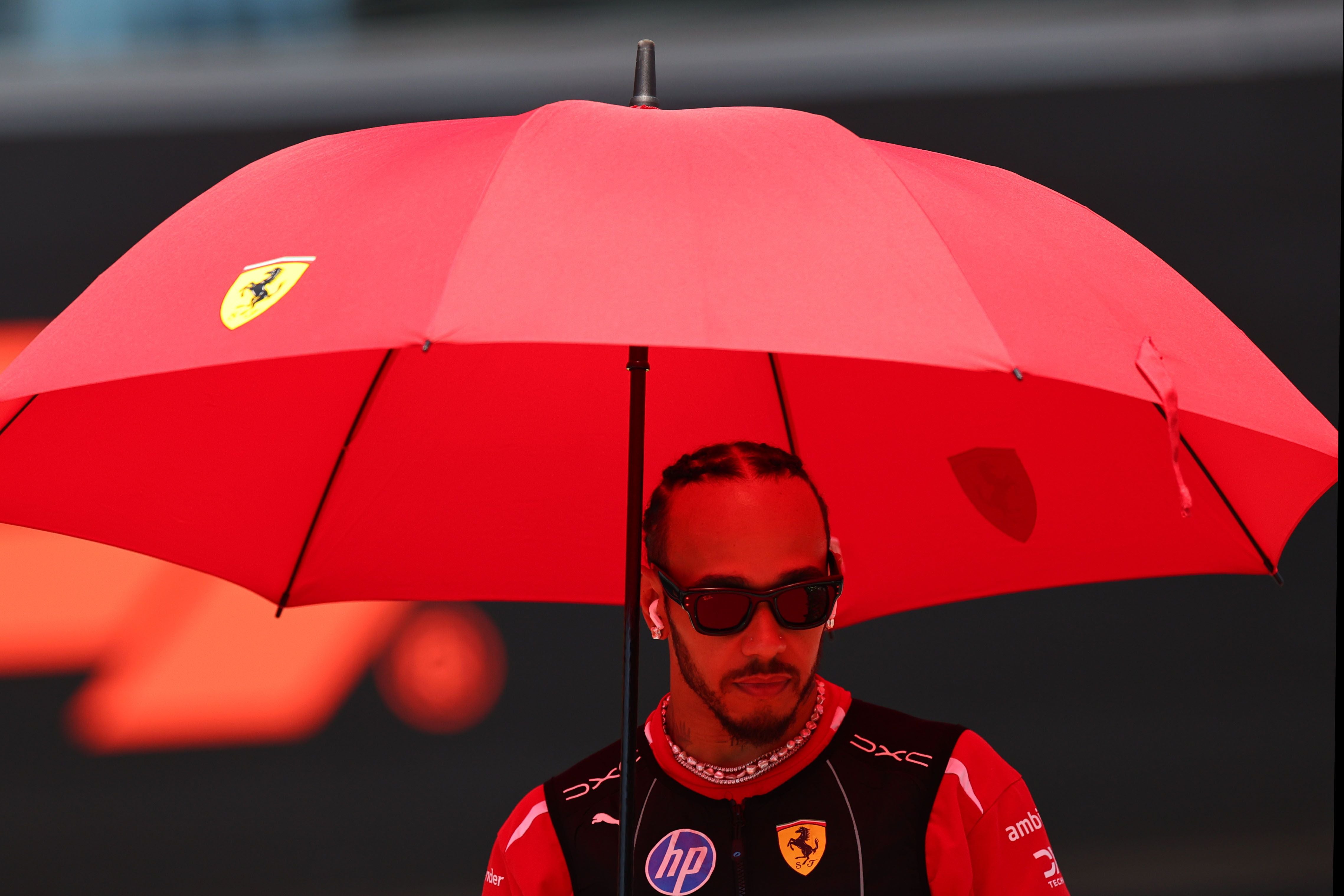 Lewis Hamilton steht mit rotem Ferrari-Schirm beim Formel-1-GP in Spielberg.