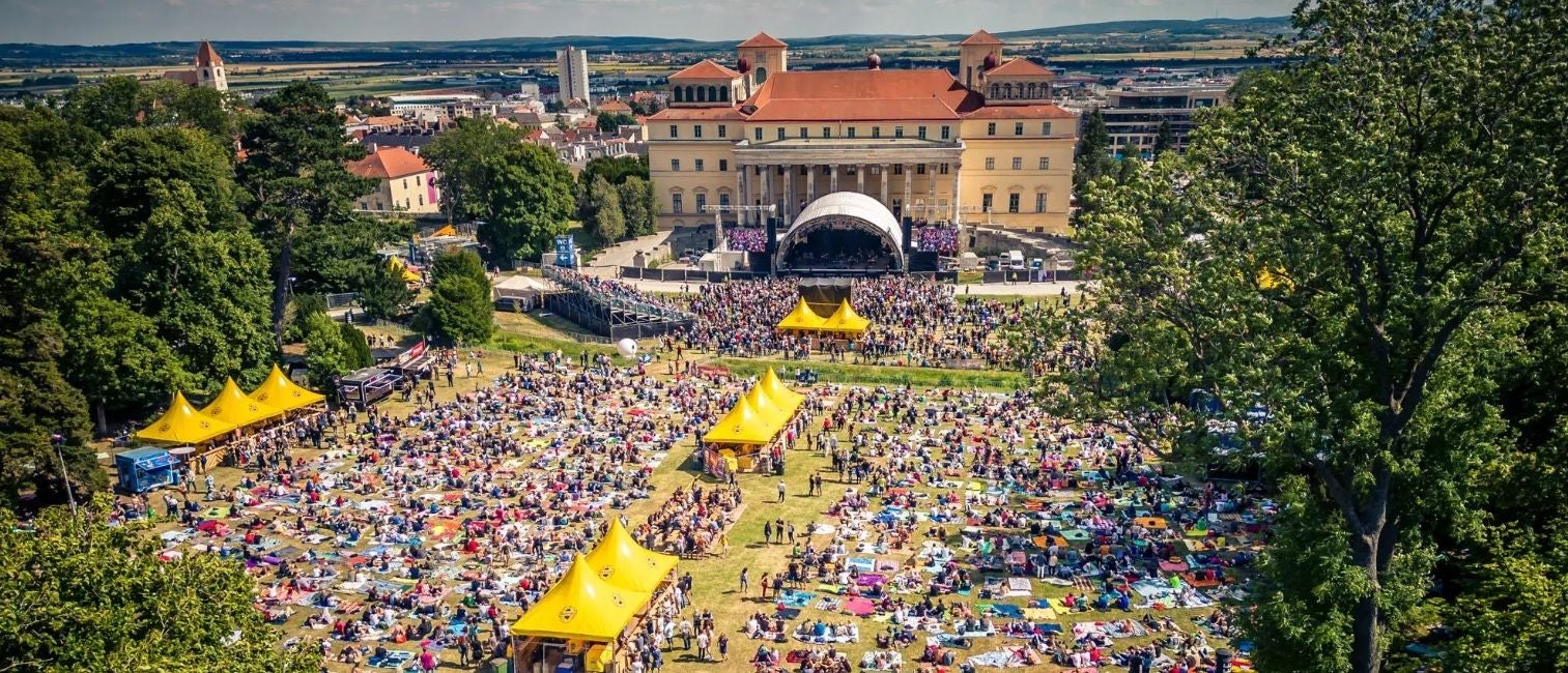 Blick auf das Forestglade Festival Eisenstadt mit Menschen, Bühne und gelben Zelten im Park.
