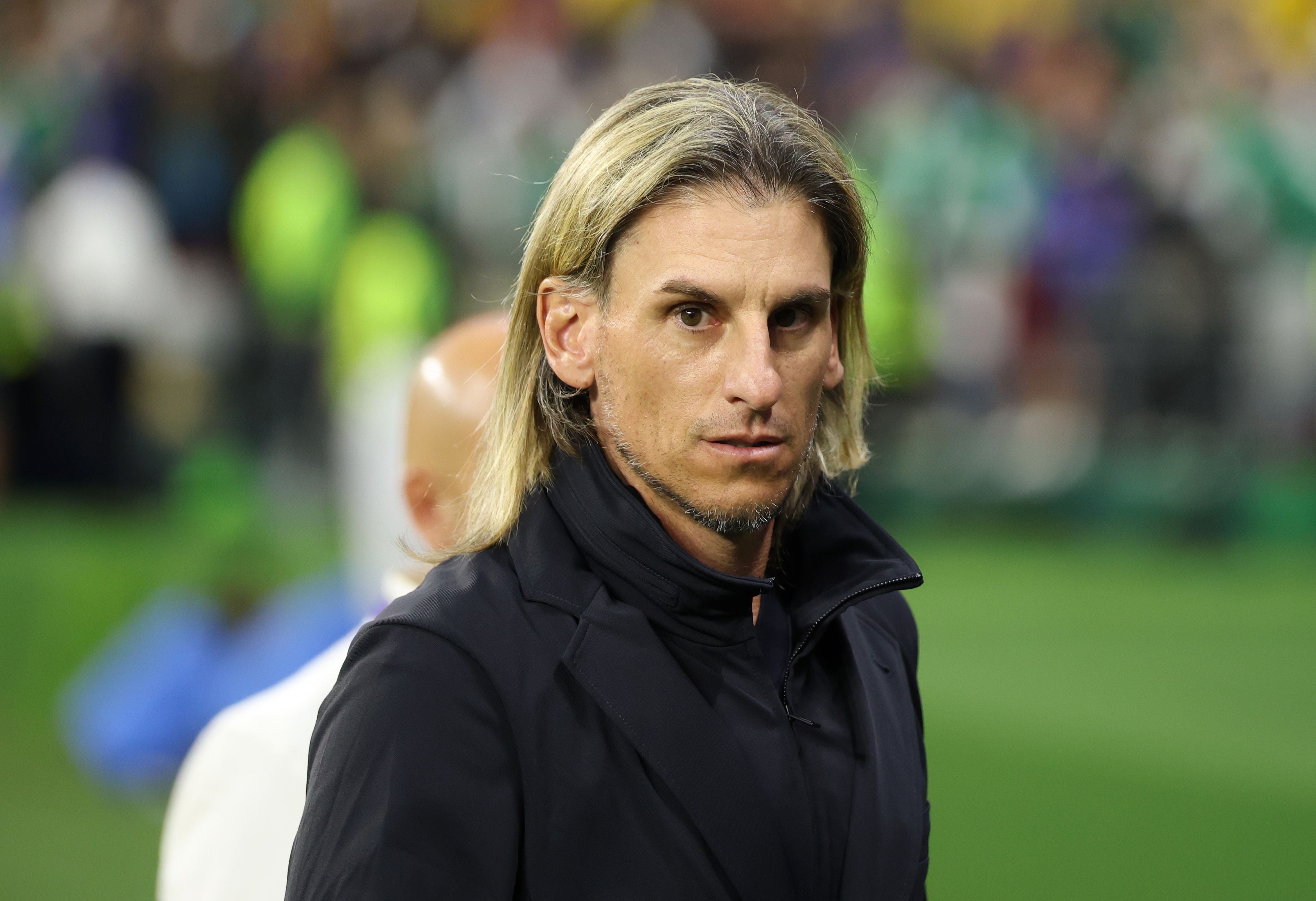 Ein Mann mit langen blonden Haaren steht im Stadion und blickt ernst in die Kamera.