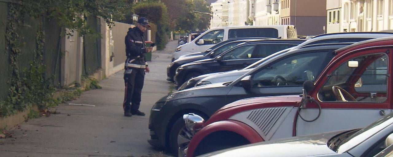 Ein Polizist kontrolliert parkende Autos am Straßenrand in einer Wohngegend.