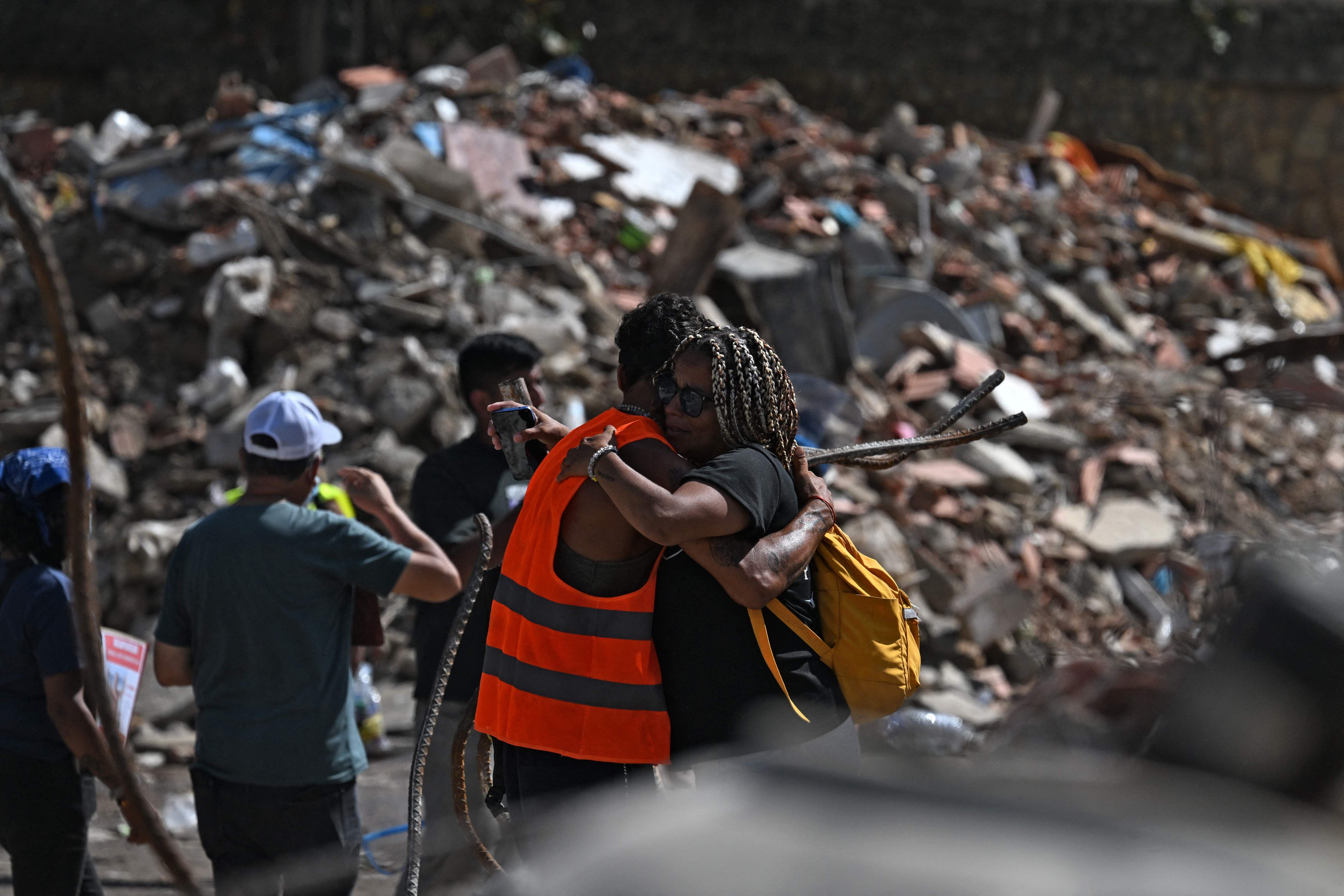 Zwei Menschen umarmen sich tröstend vor Trümmern nach einem Erdbeben in Venezuela.
