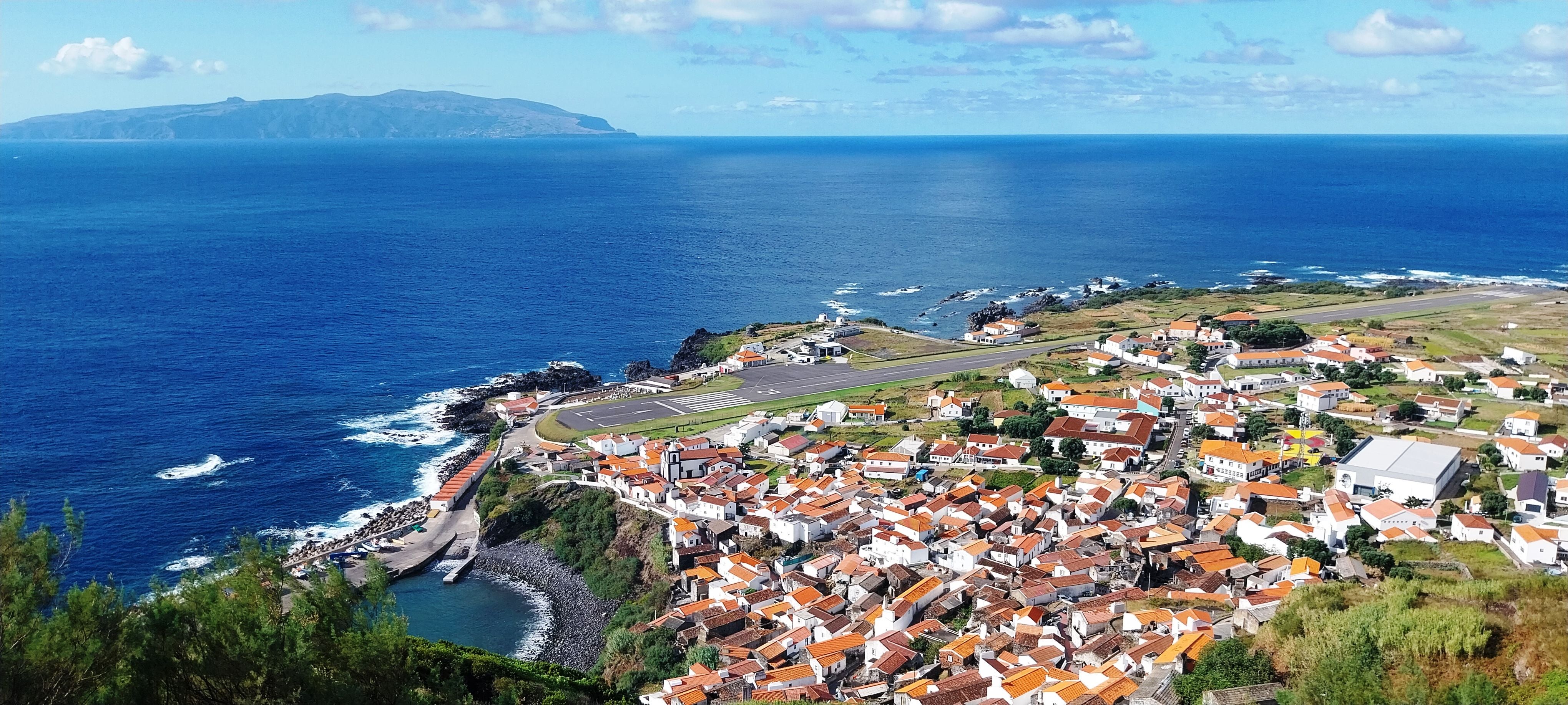 Panorama von Corvo mit Stadt, Flughafen am Meer und Flores-Insel im Hintergrund.