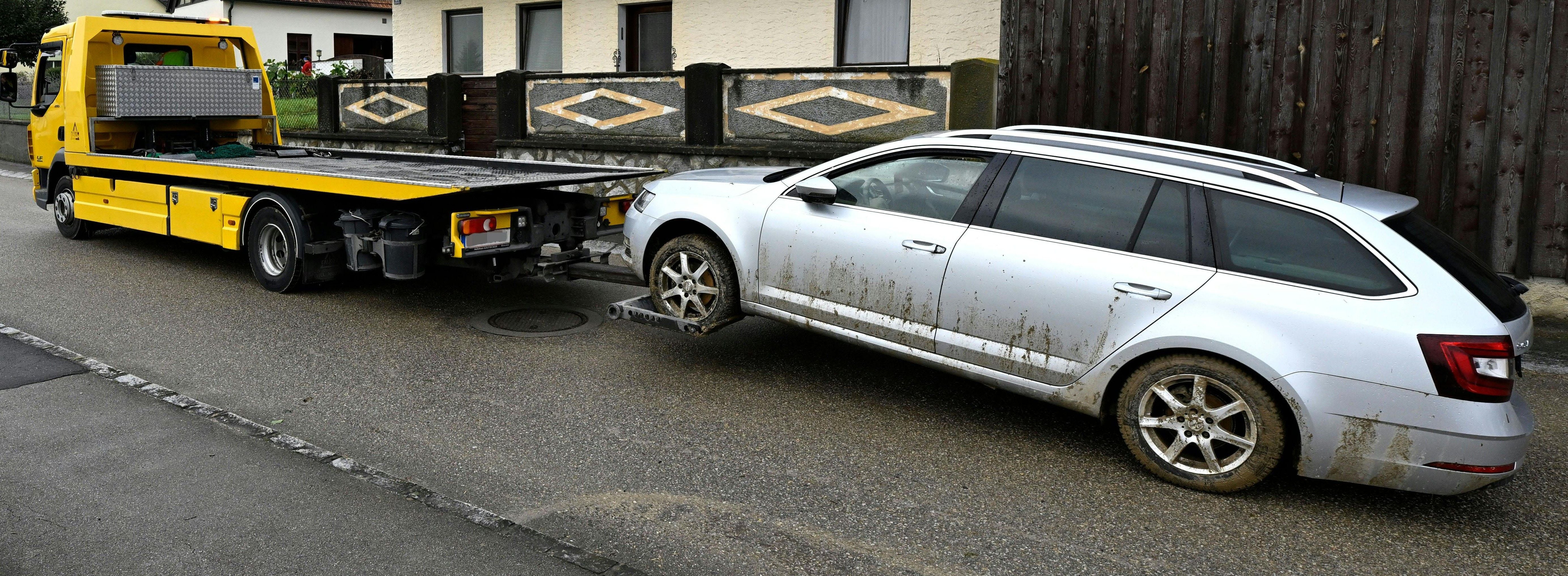 Ein gelber Abschleppwagen schleppt einen verschmutzten silbernen Kombi auf einer Straße ab.