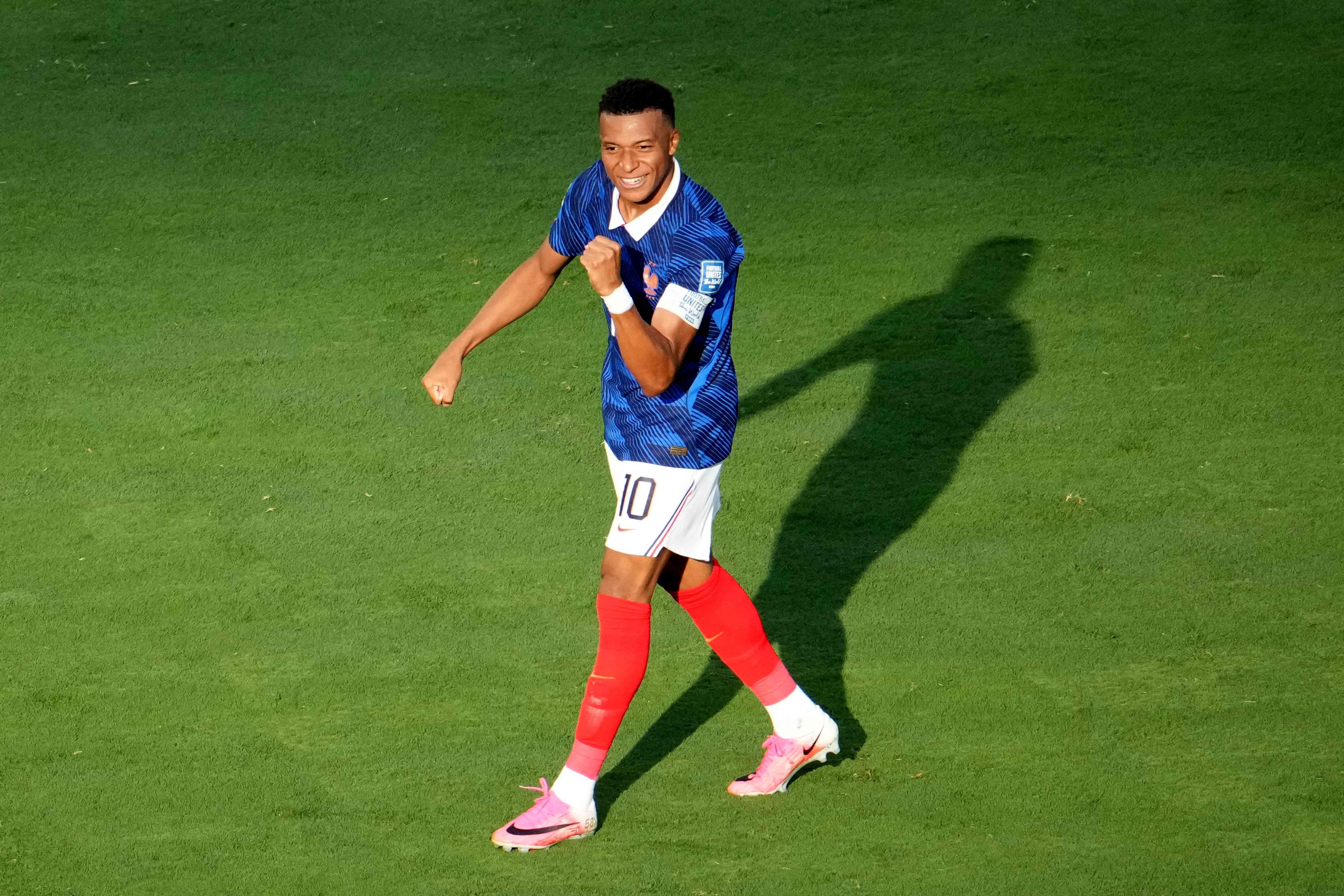 Ein Fußballspieler im blauen Trikot jubelt lachend auf dem Spielfeld.