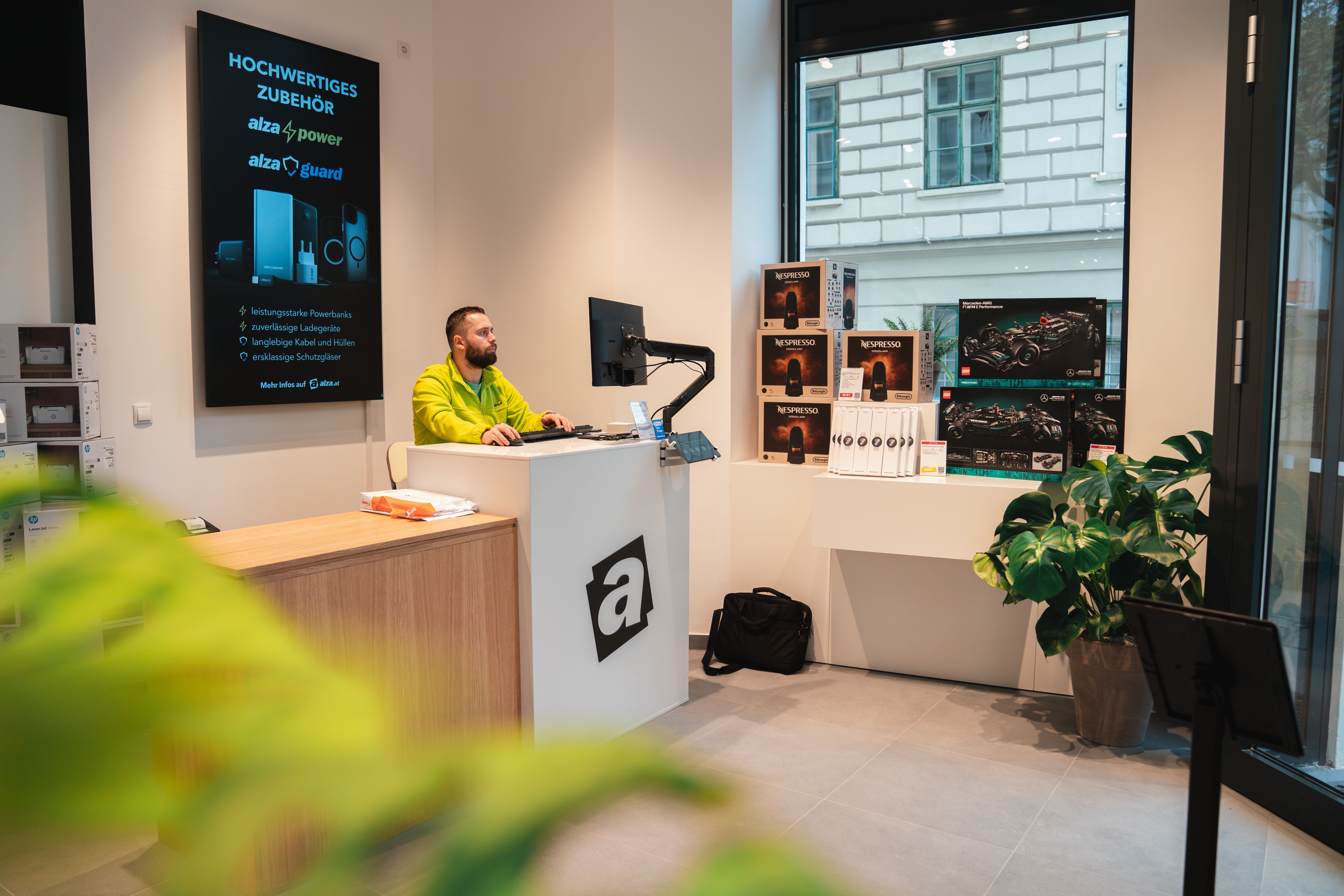 Ein Mitarbeiter sitzt an einem Computer in einem modernen Alza-Shop mit Elektronikprodukten.