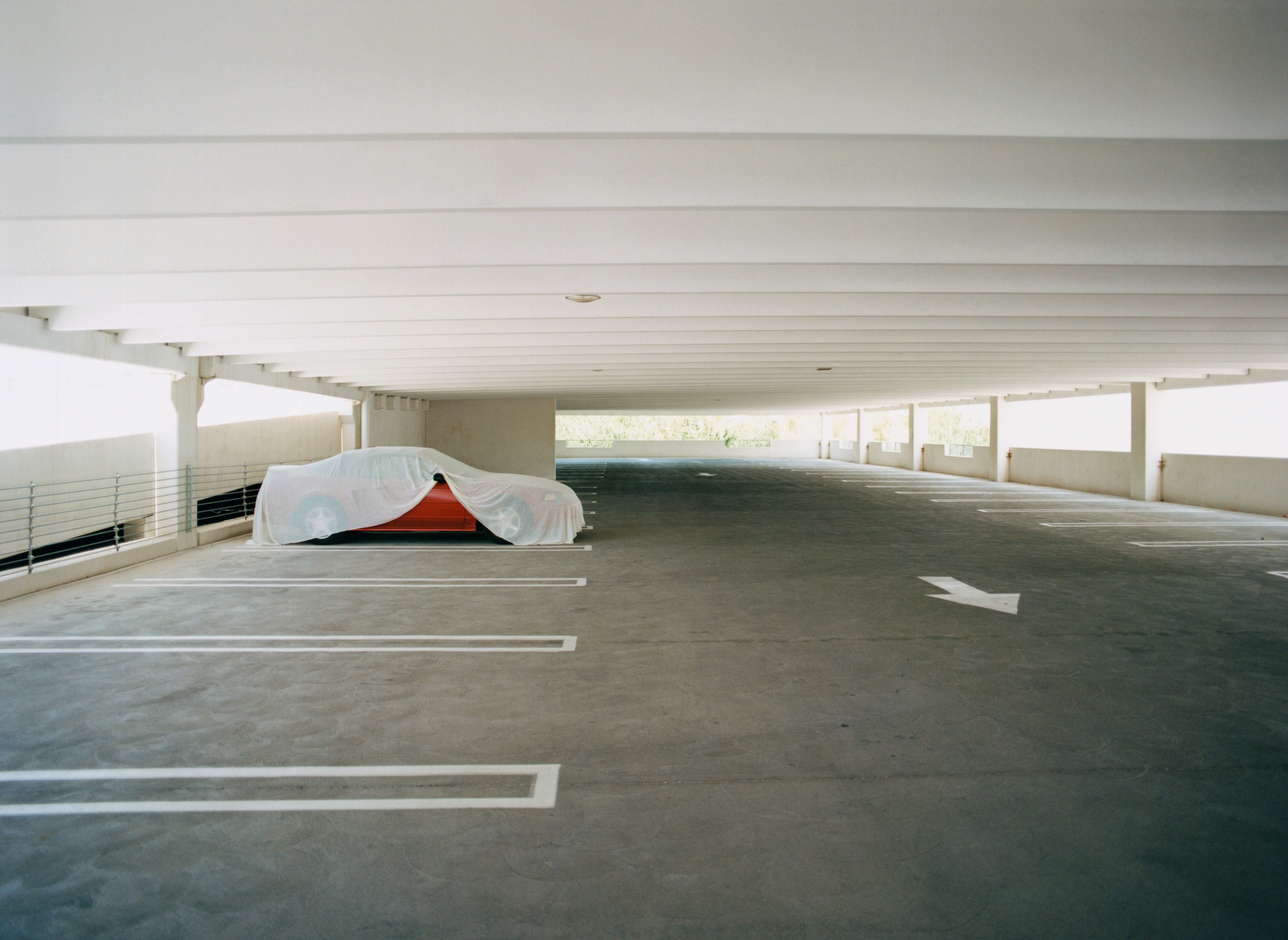 Leeres Parkhaus mit einem rot abgedeckten Auto in einer Ecke.