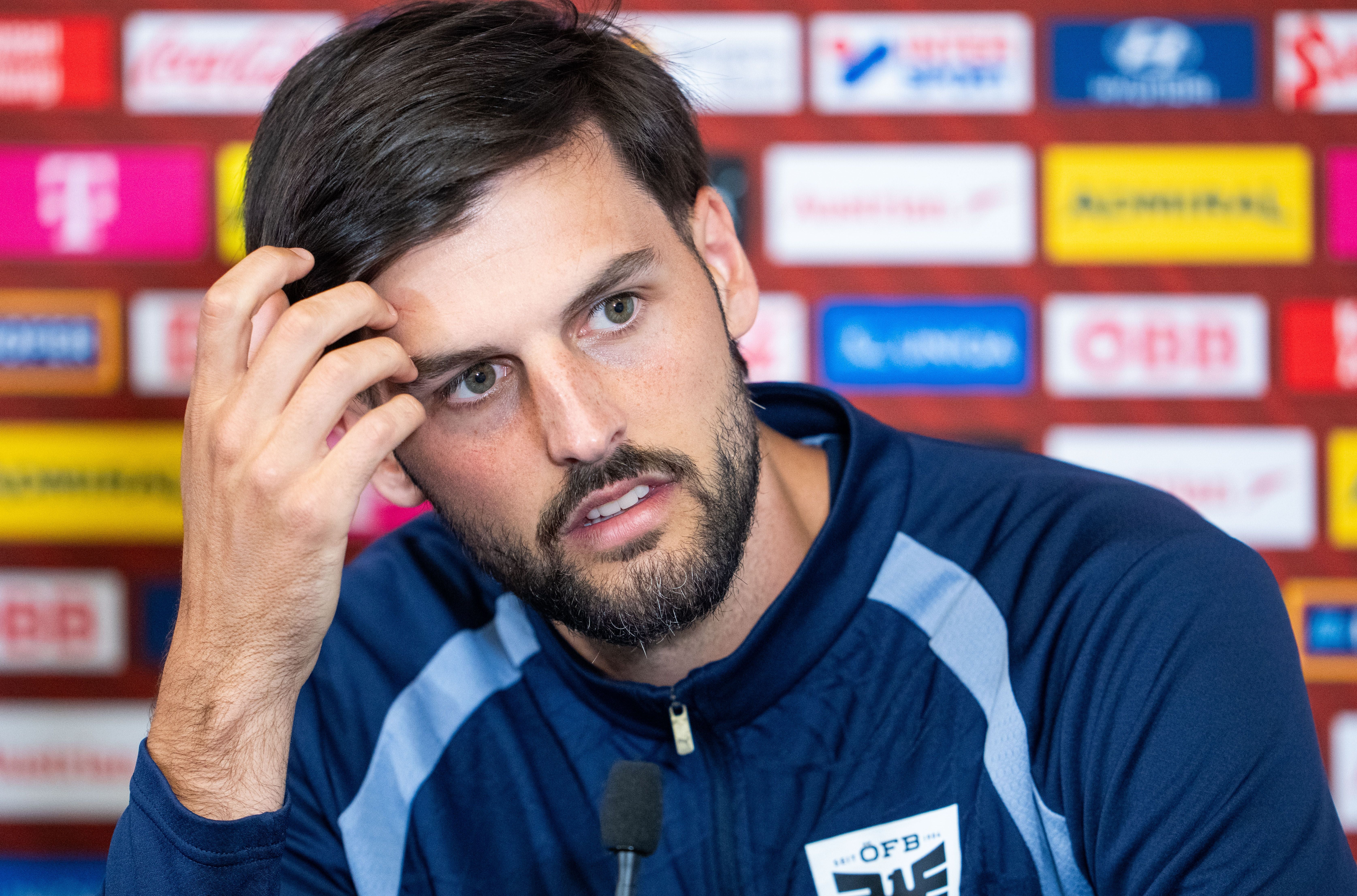 Ein Mann im blauen Trainingsanzug spricht nachdenklich bei einer Pressekonferenz.