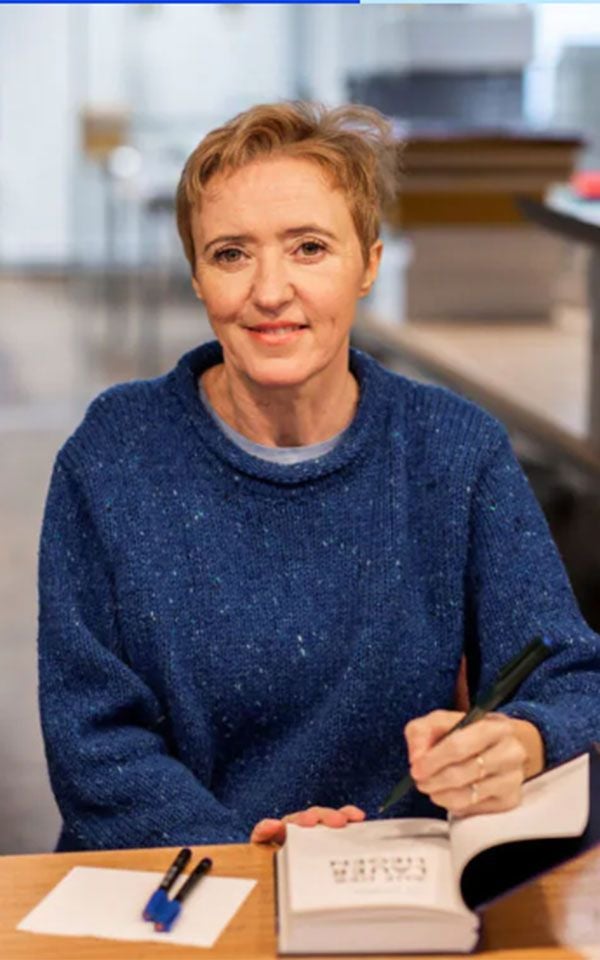 Frau mit kurzem Haar signiert ein Buch und lächelt in die Kamera.