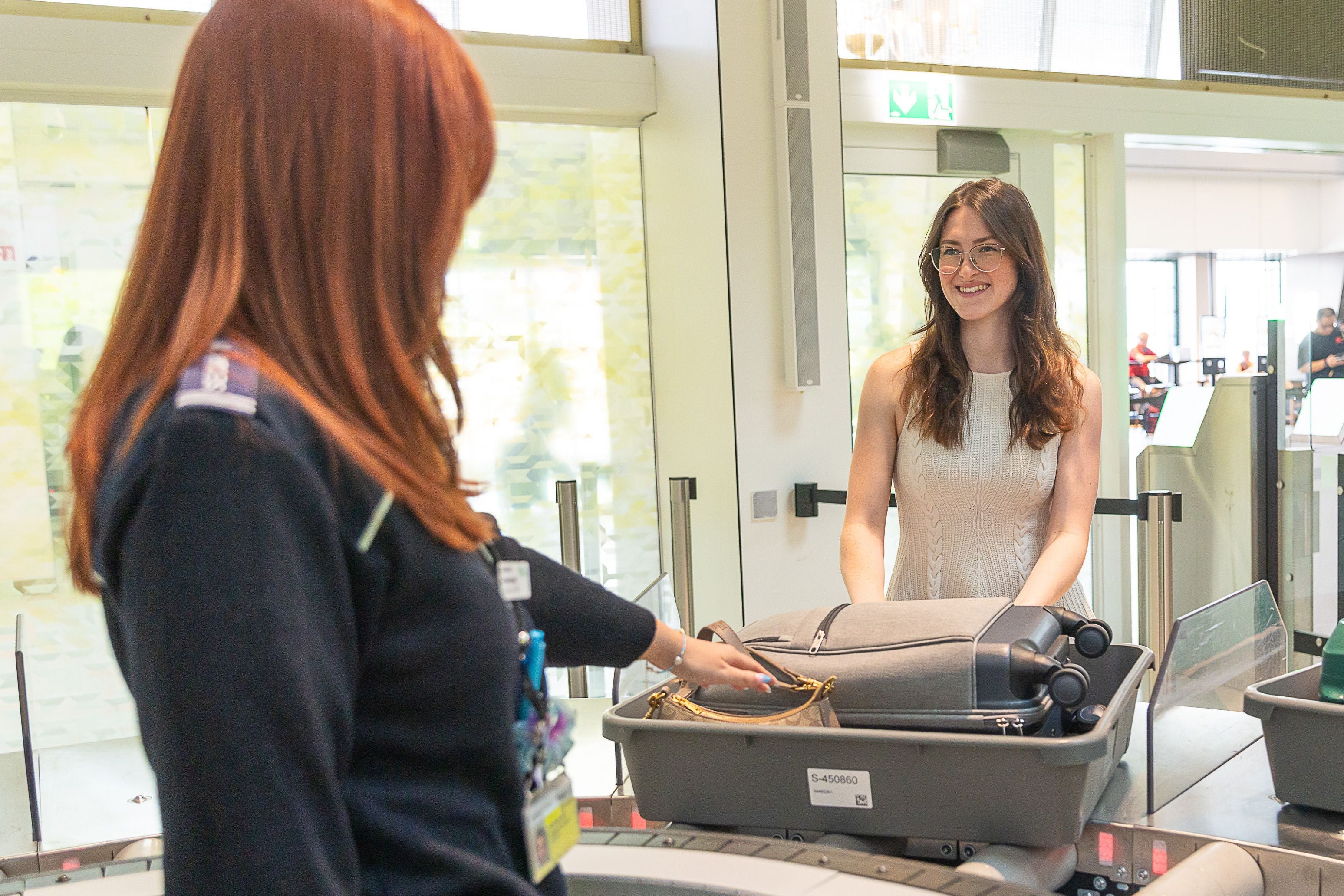 Eine Frau legt ihr Gepäck am Flughafen-Scanner ab, während eine Sicherheitskraft kontrolliert.