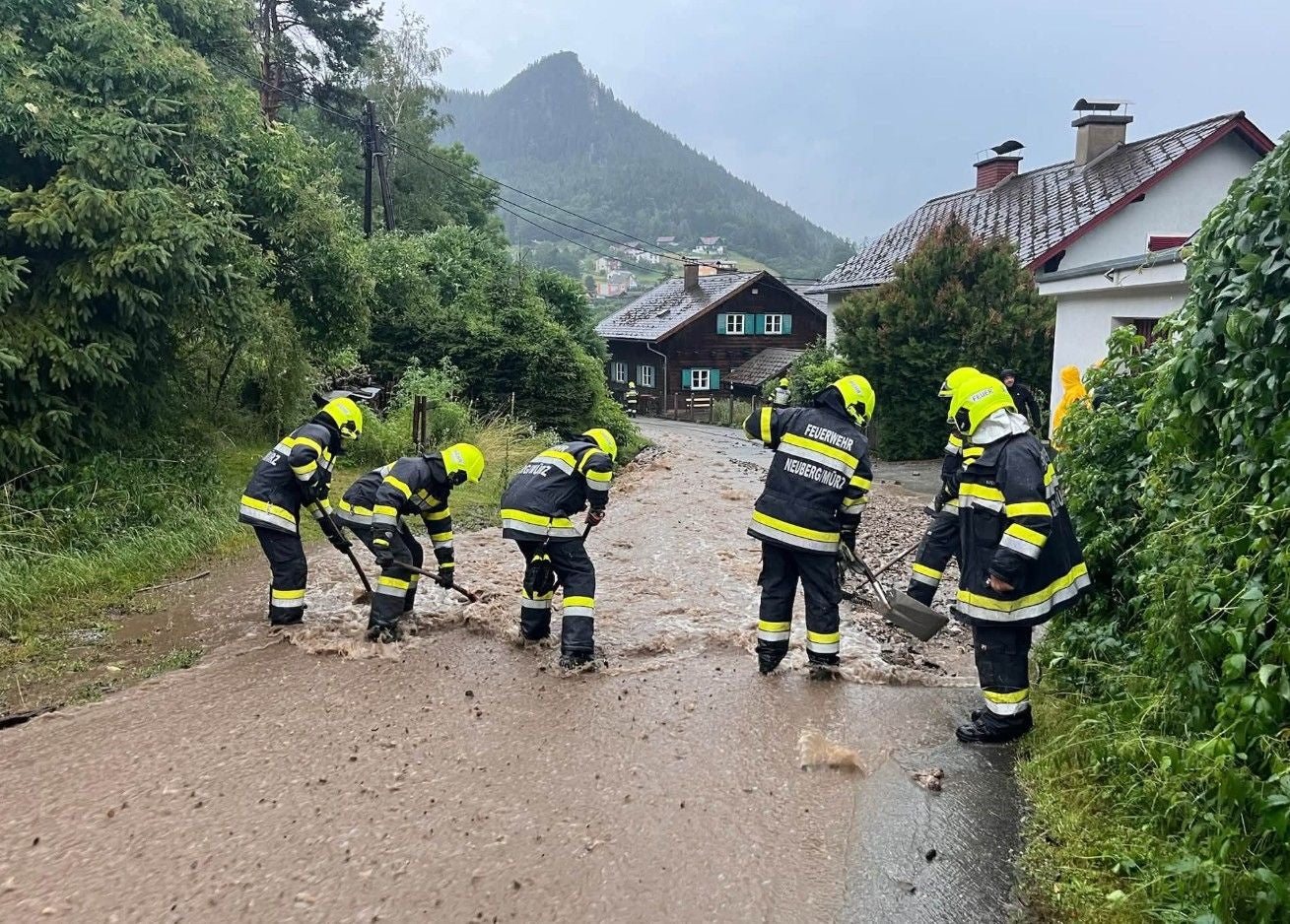Feuerwehrleute beseitigen bei starkem Regen Schlamm von einer überfluteten Straße in Neuberg an der Mürz.
