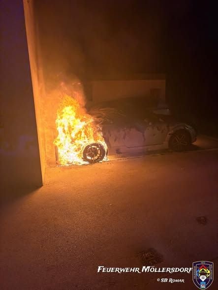 Ein Auto brennt an der Vorderseite neben einer Hauswand in der Nacht.