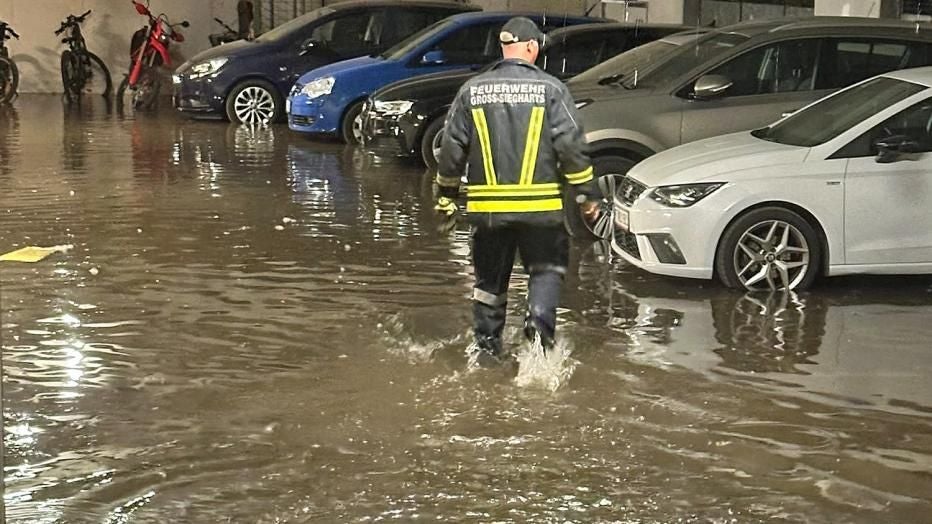 Ein Feuerwehrmann läuft durch eine überflutete Tiefgarage mit parkenden Autos und spiegelndem Wasser.