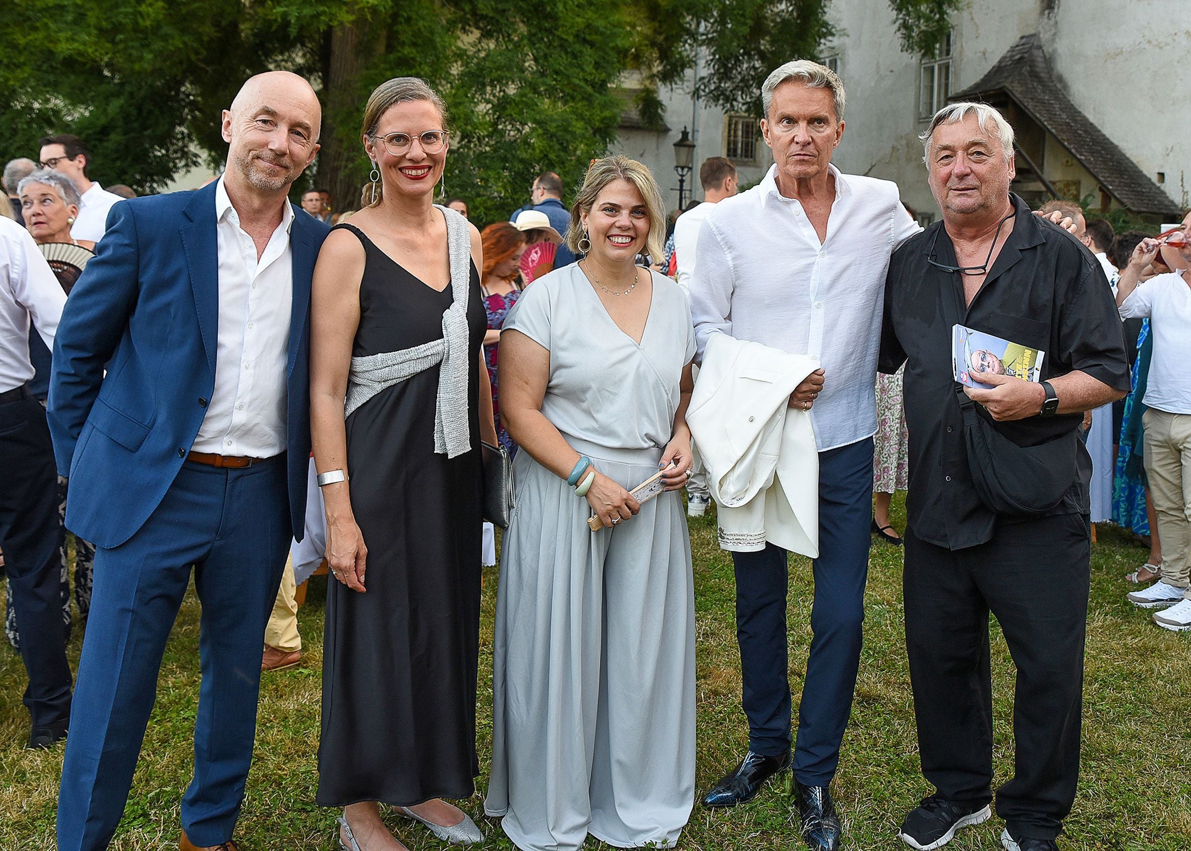 Fünf elegant gekleidete Personen stehen im Freien bei einer Veranstaltung zusammen.