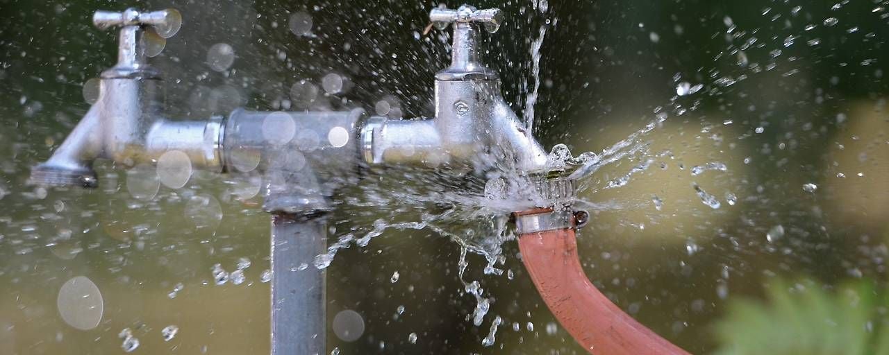 Wasser spritzt aus einer undichten Verbindung zwischen Wasserhahn und Gartenschlauch.