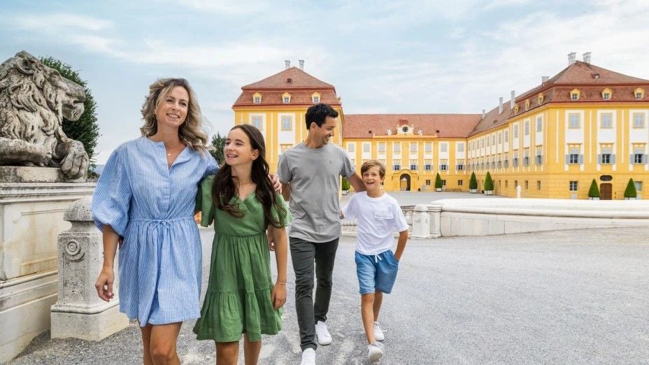 Eine Familie spaziert fröhlich im Schlosshof von Schloss Hof bei sonnigem Wetter.