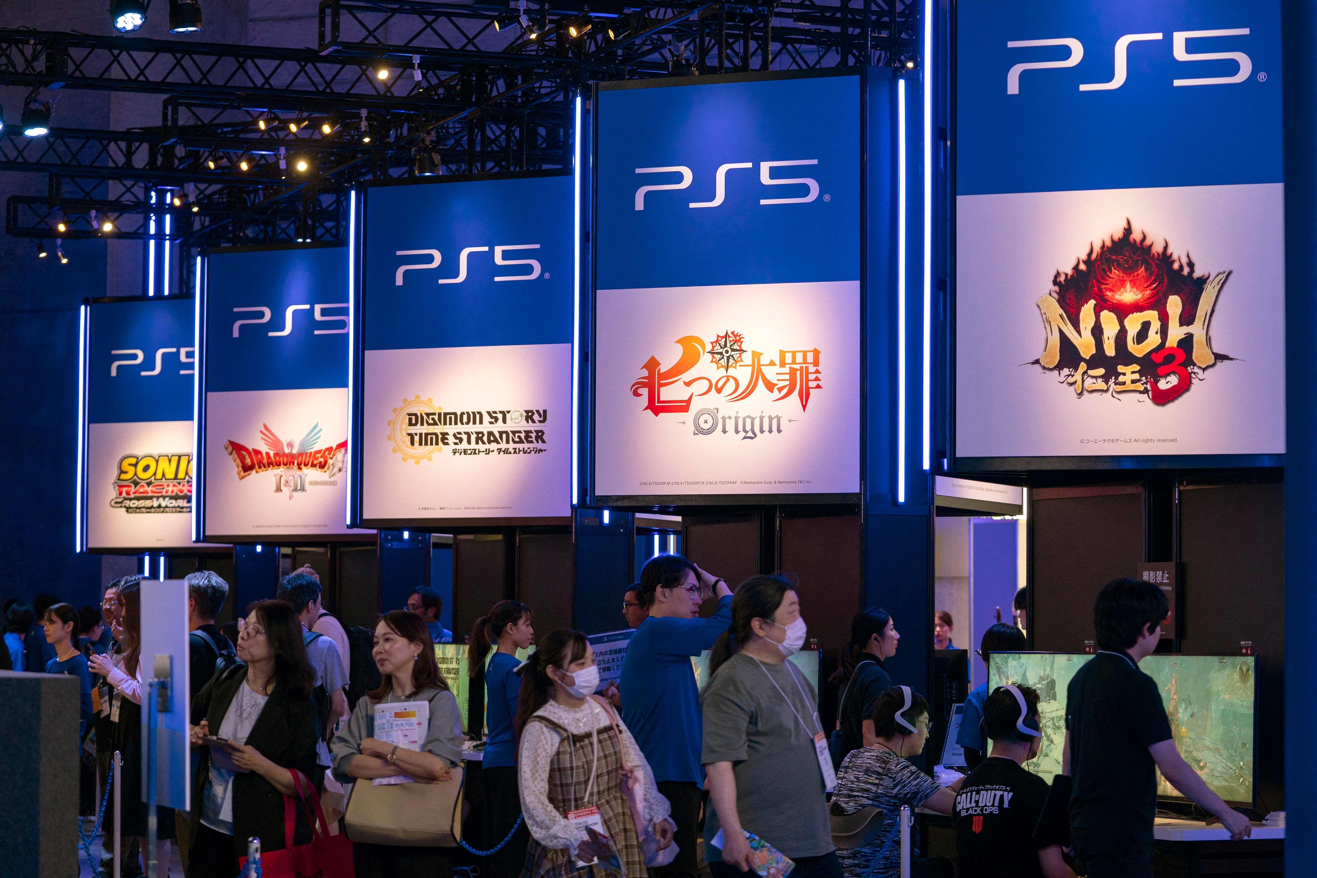 Menschen stehen und sitzen an PS5-Spielständen auf einer Spielemesse mit leuchtenden Displays.