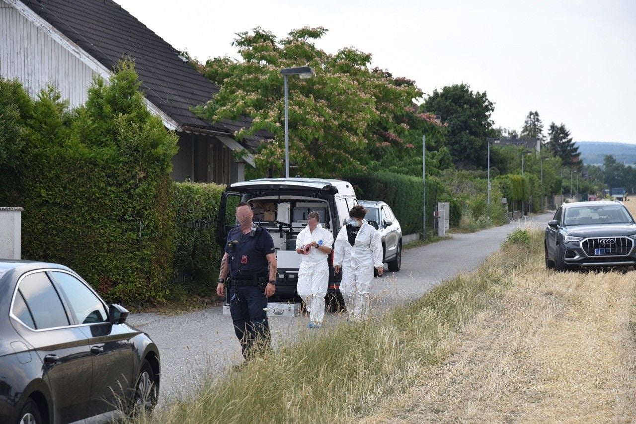 Polizist und Forensiker in Schutzanzügen stehen vor einem Haus und einem Einsatzfahrzeug.