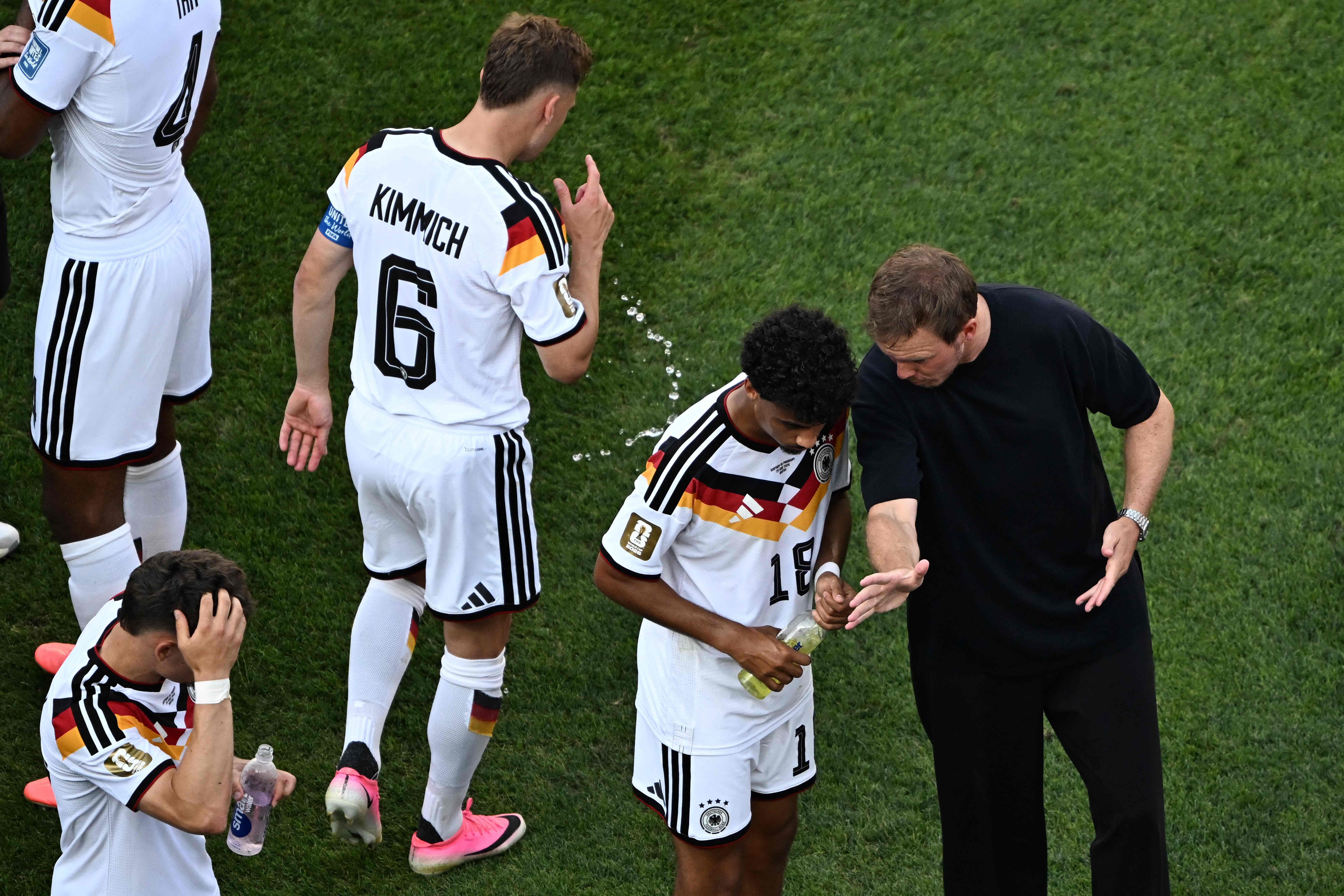 Trainer spricht während einer Pause mit deutschem Spieler auf dem Fußballfeld, andere stehen daneben.