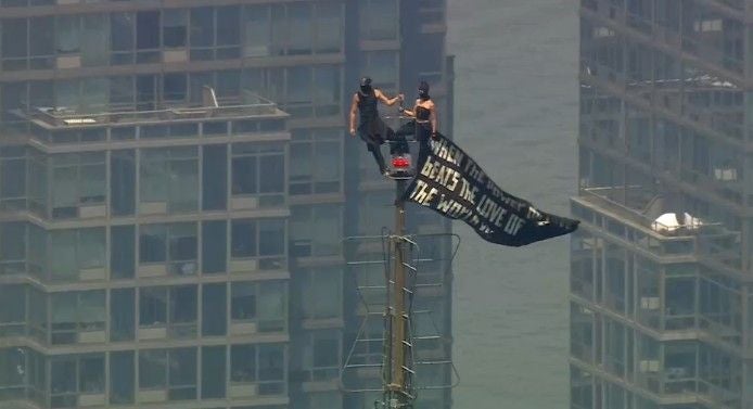 Zwei Personen klettern auf die Spitze des Empire State Buildings und hissen einen großen schwarzen Banner.