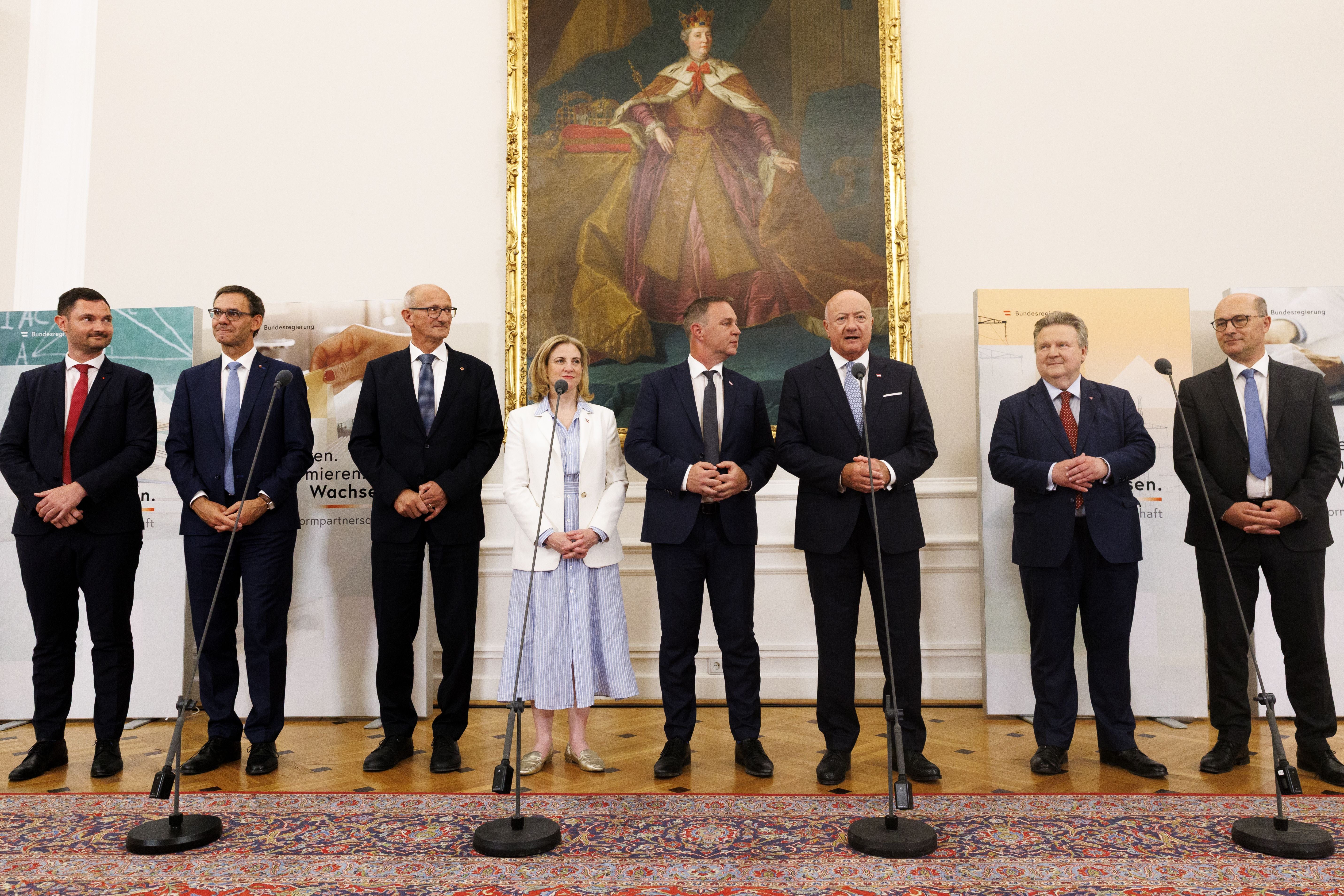 Acht Personen stehen bei einer Pressekonferenz im Bundeskanzleramt Wien vor einem Gemälde.