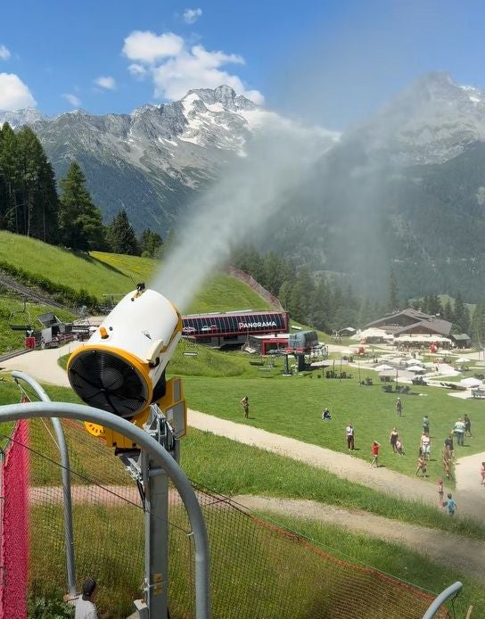 Beschneiungsanlage sprüht Wasser im Sommer, Menschen und Berge im Hintergrund, Skiworld Ahrntal.