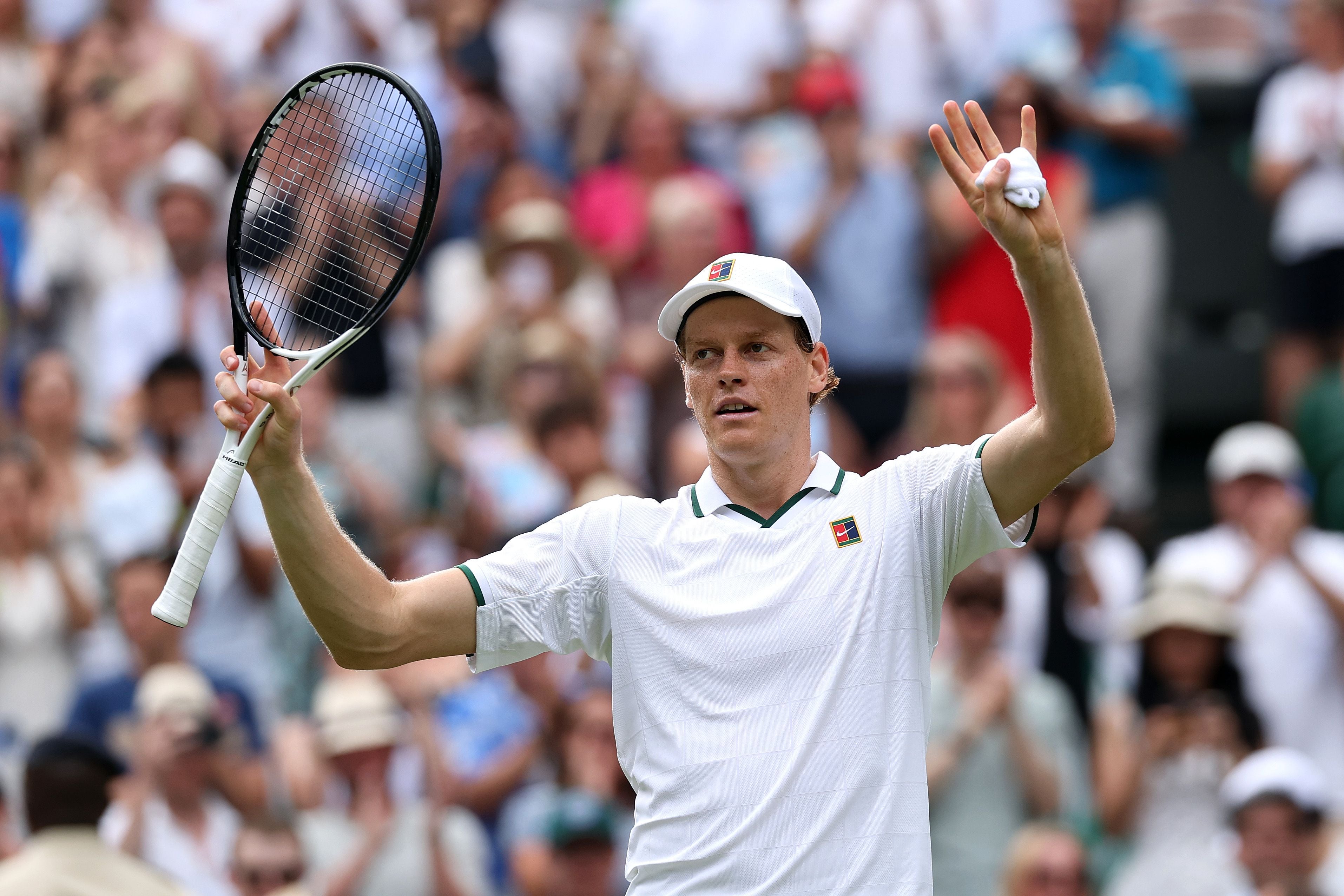 Tennisspieler im weißen Outfit jubelt mit erhobenen Armen auf dem Tennisplatz vor Publikum.
