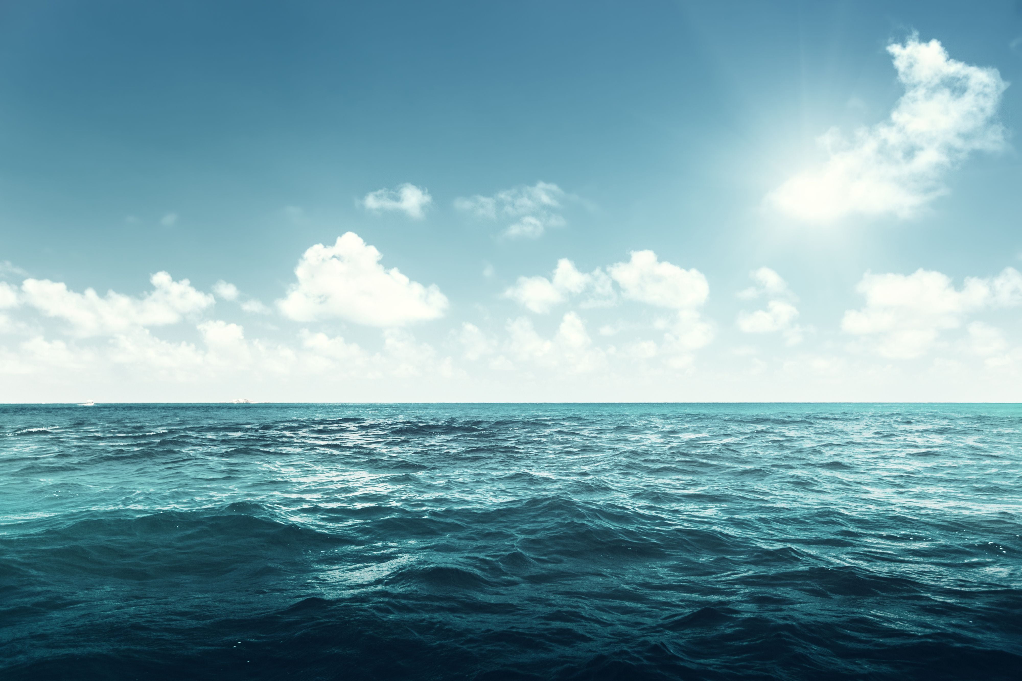 Blaues Meer unter klarem Himmel mit einigen weißen Wolken und Sonnenschein.
