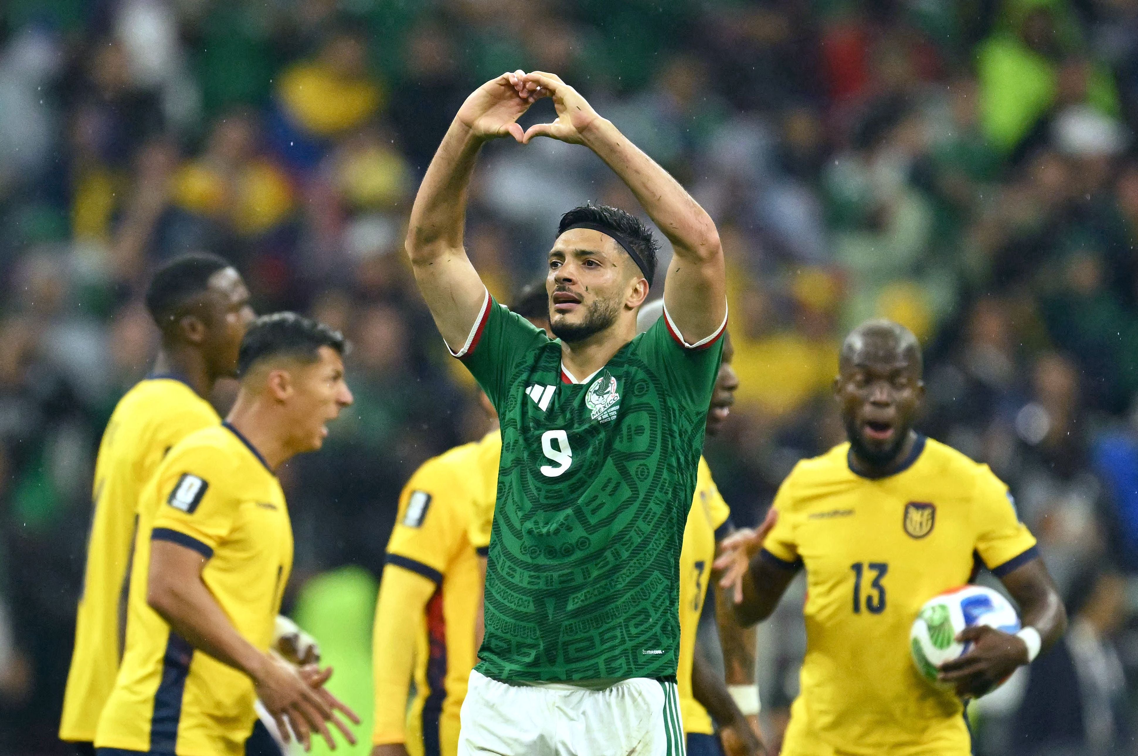 Ein mexikanischer Fußballspieler jubelt mit einem Herzzeichen, Spieler aus Ecuador im Hintergrund.